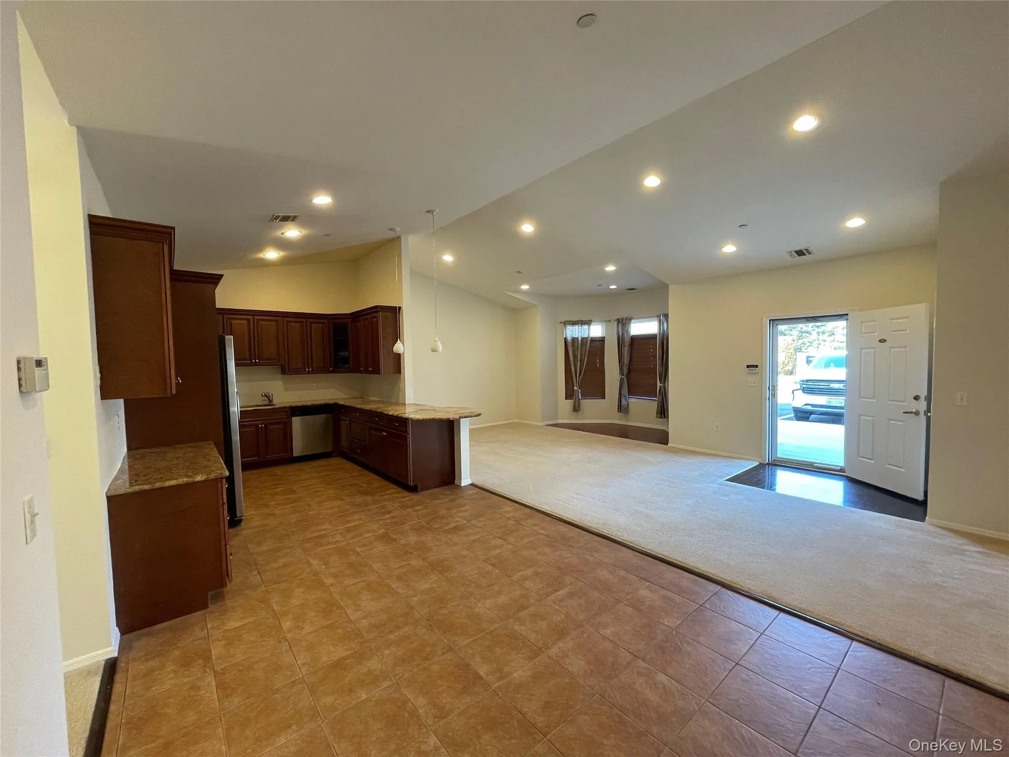 Kitchen featuring open floor plan, a peninsula, vaulted ceiling, light stone counters, and glass insert cabinets Kitchen featuring open floor plan, a peninsula, vaulted ceiling, light stone counters, and glass insert cabinets