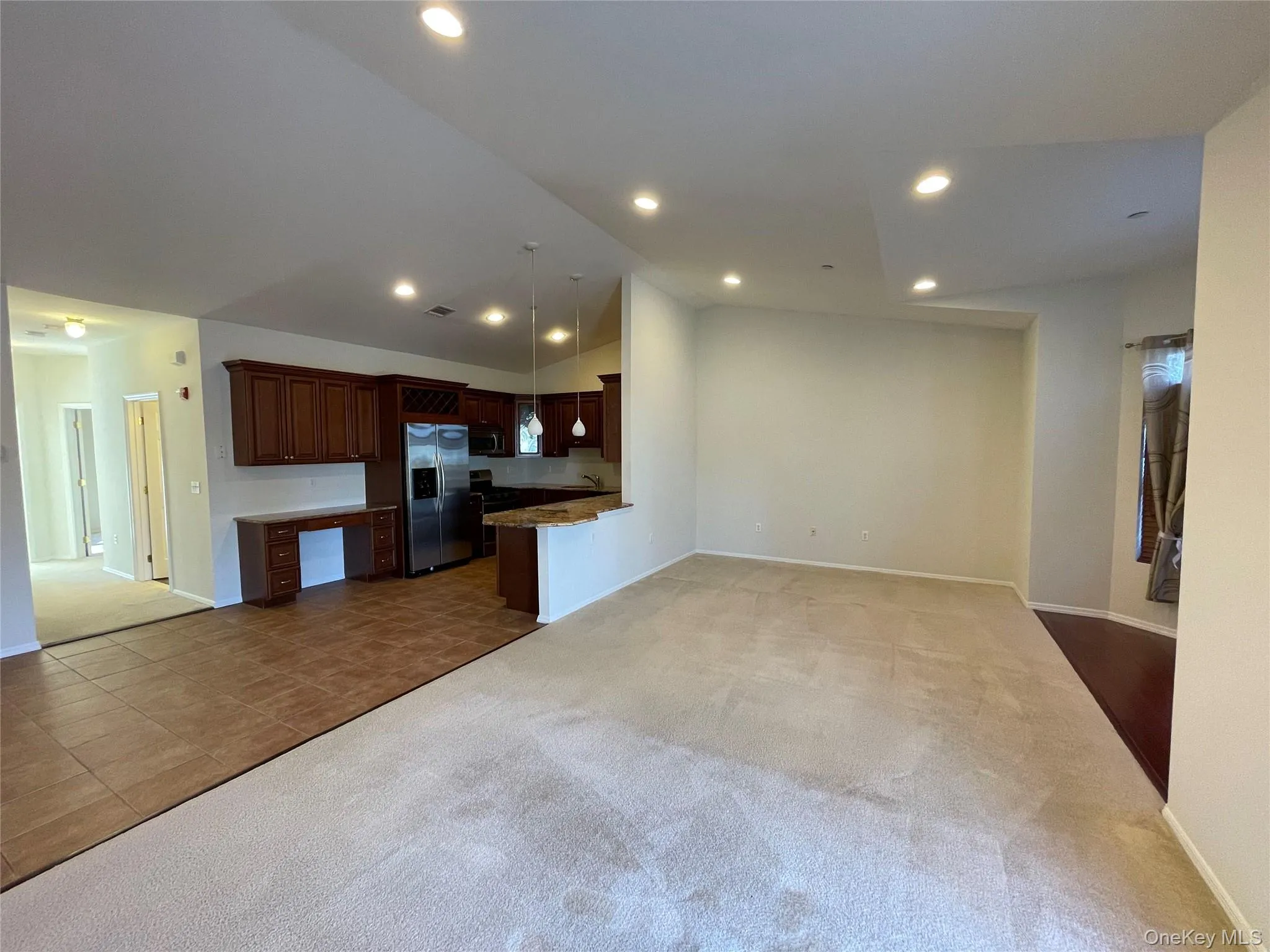 Kitchen featuring dark colored carpet, open floor plan, lofted ceiling, appliances with stainless steel finishes, and dark brown cabinetry Kitchen featuring dark colored carpet, open floor plan, lofted ceiling, appliances with stainless steel finishes, and dark brown cabinetry