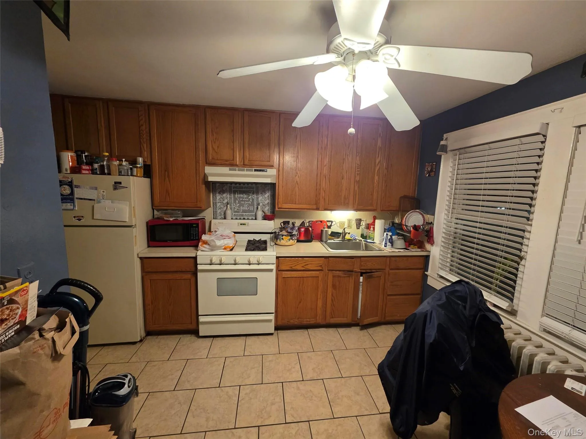 Kitchen featuring brown cabinets, white appliances, light countertops, ceiling fan, and under cabinet range hood Kitchen featuring brown cabinets, white appliances, light countertops, ceiling fan, and under cabinet range hood