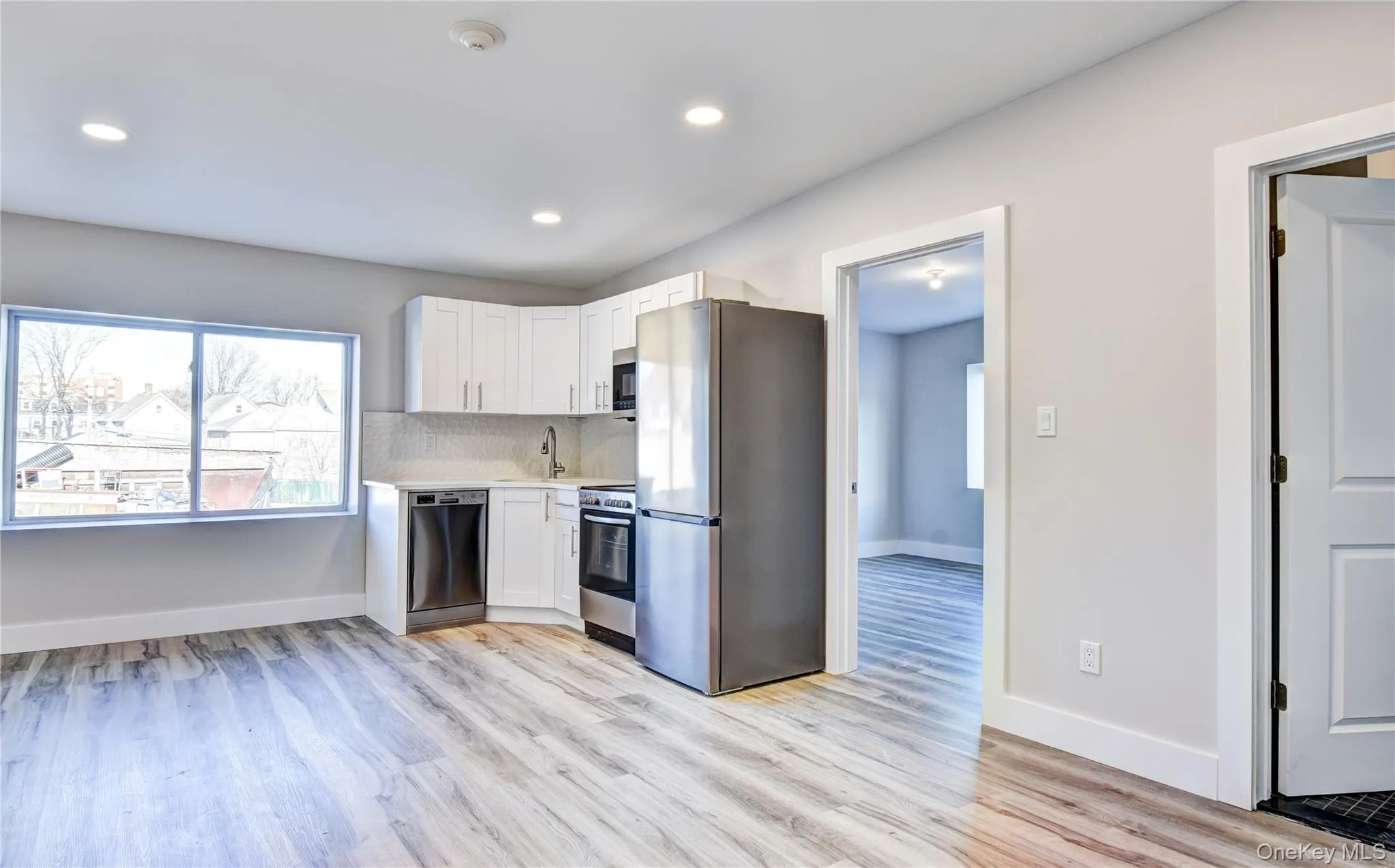 Kitchen with appliances with stainless steel finishes, white cabinets, tasteful backsplash, light wood finished floors, and light stone countertops Kitchen with appliances with stainless steel finishes, white cabinets, tasteful backsplash, light wood finished floors, and light stone countertops