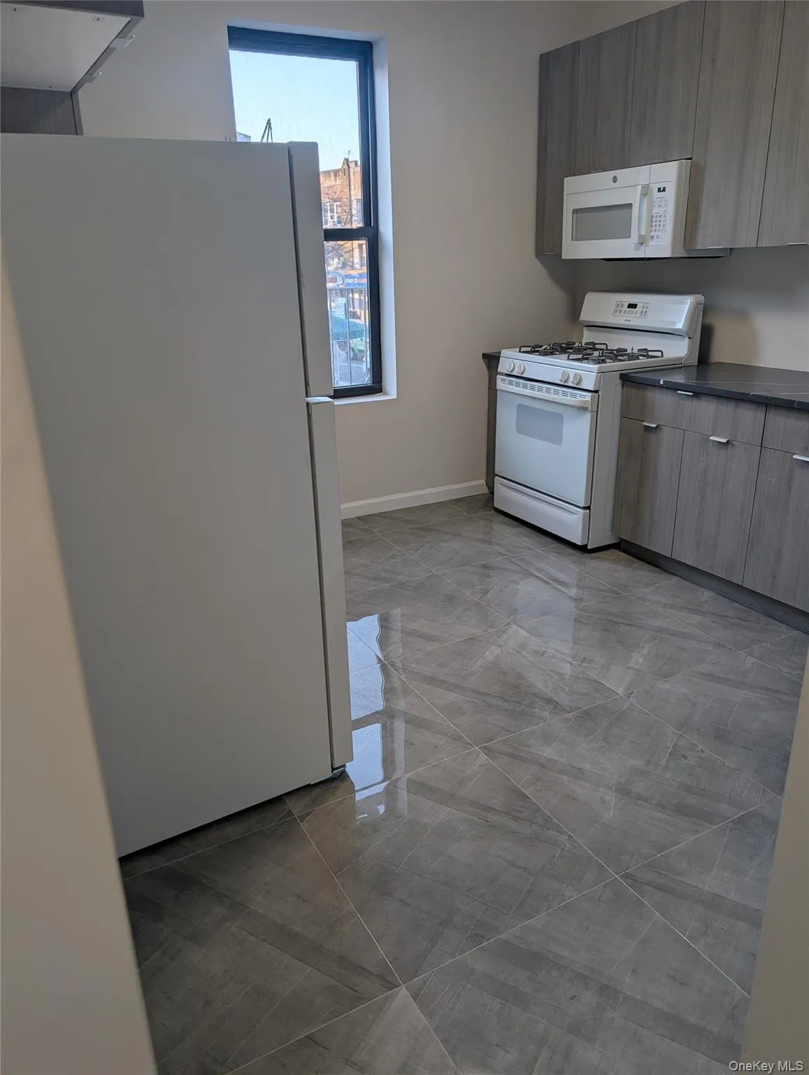 Kitchen with white appliances, light marble finish floors, dark countertops, and modern cabinets Kitchen with white appliances, light marble finish floors, dark countertops, and modern cabinets
