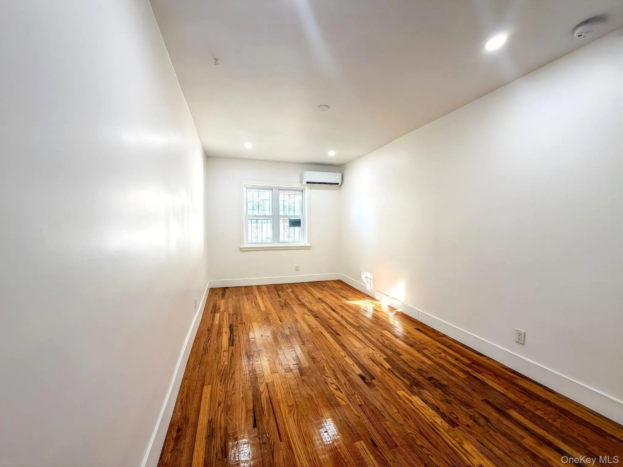 Empty room with hardwood / wood-style floors, recessed lighting, and a wall mounted air conditioner Empty room with hardwood / wood-style floors, recessed lighting, and a wall mounted air conditioner
