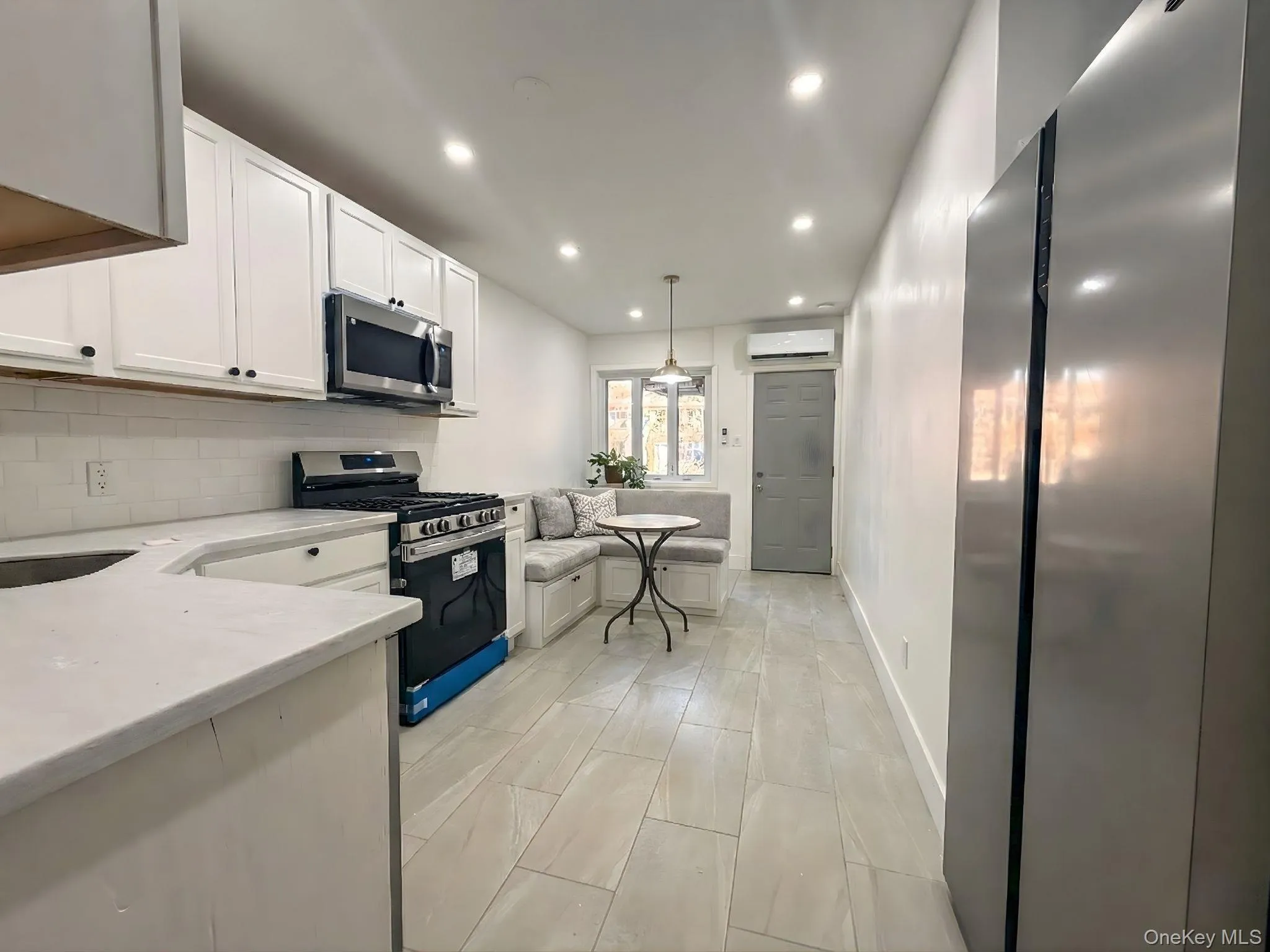 Kitchen featuring stainless steel appliances, white cabinetry, recessed lighting, light stone countertops, and decorative light fixtures Kitchen featuring stainless steel appliances, white cabinetry, recessed lighting, light stone countertops, and decorative light fixtures