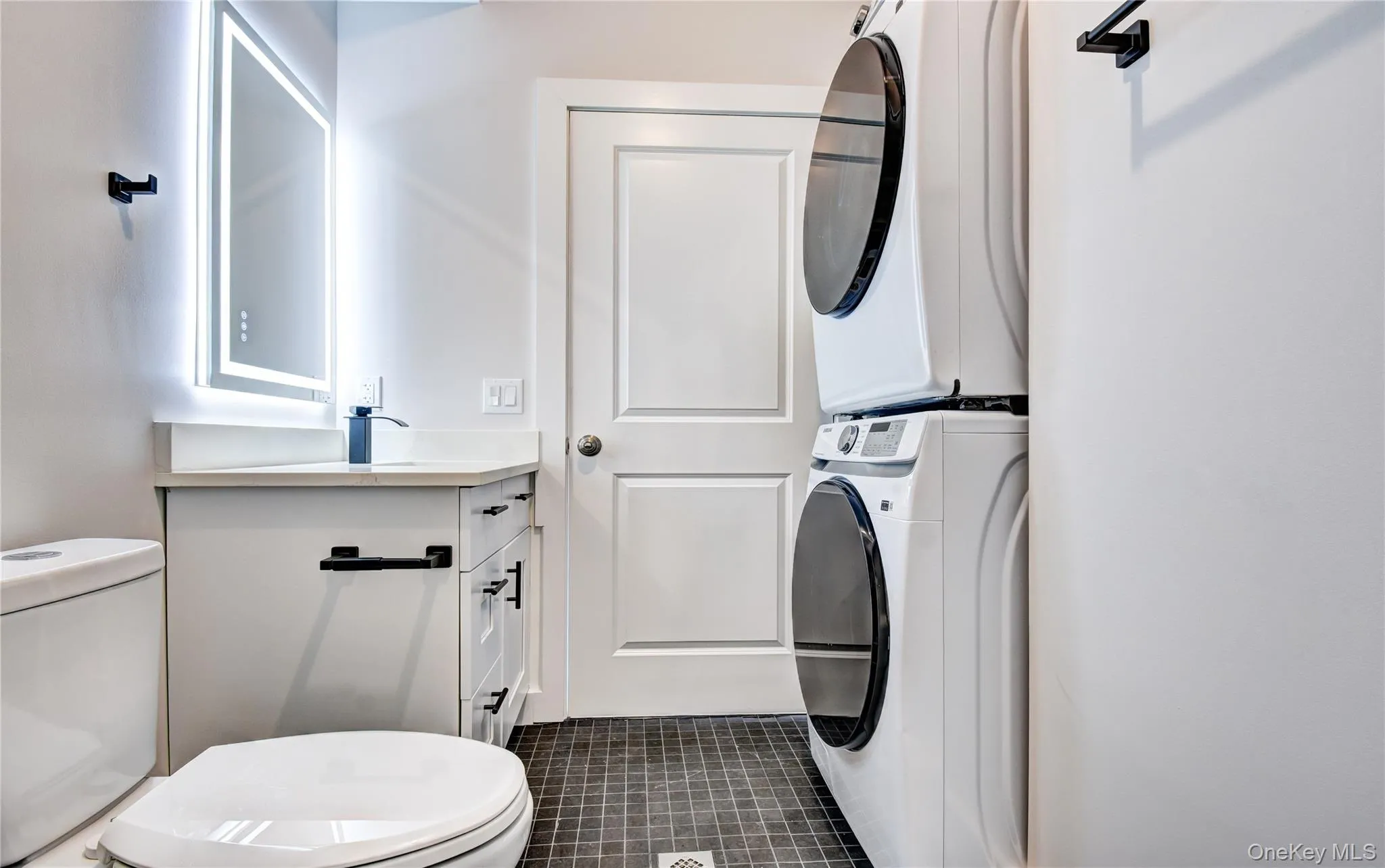 Half bath featuring vanity, stacked washing machine and dryer, and dark tile patterned flooring Half bath featuring vanity, stacked washing machine and dryer, and dark tile patterned flooring