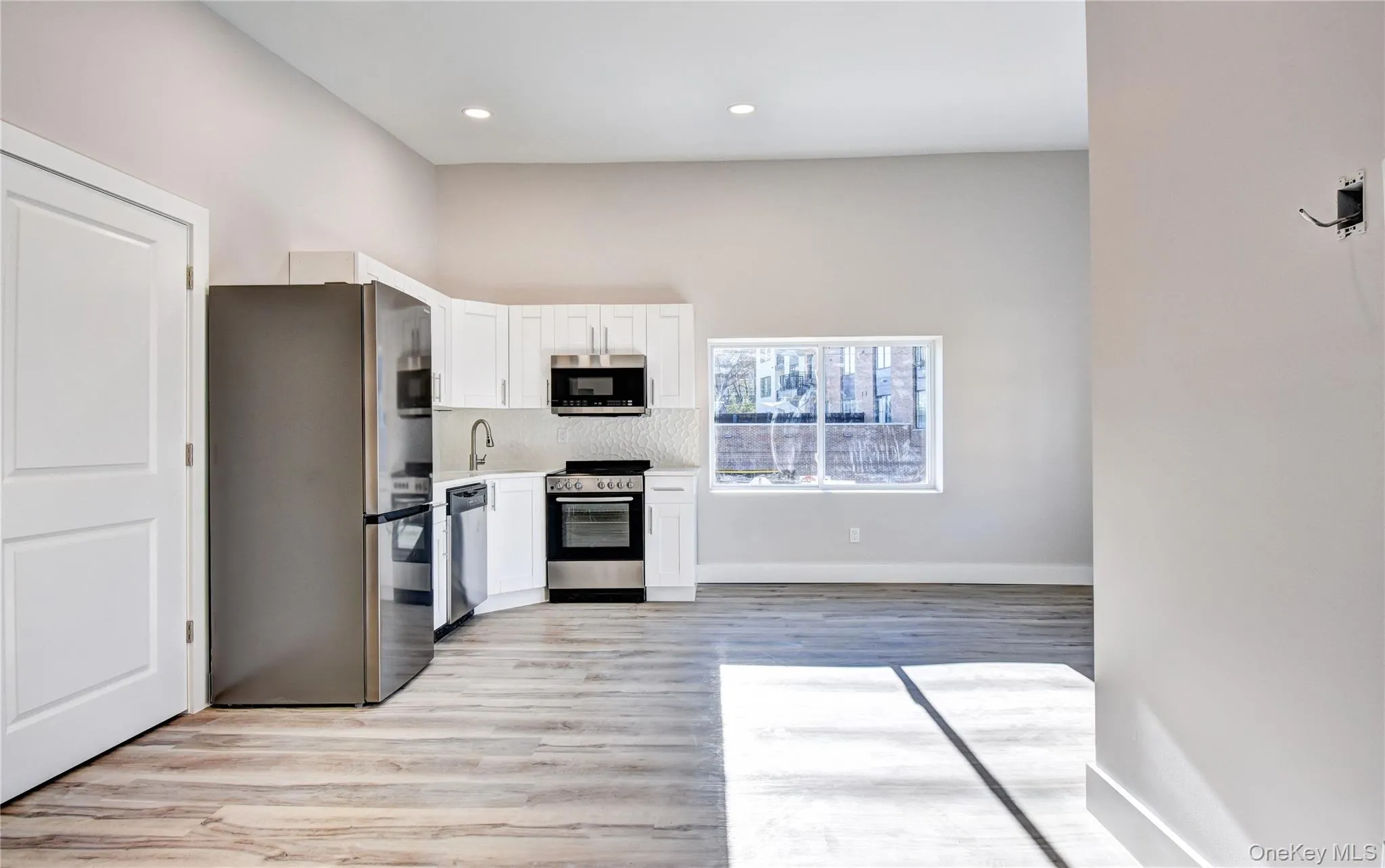 Kitchen with stainless steel appliances, white cabinetry, light wood-style flooring, decorative backsplash, and recessed lighting Kitchen with stainless steel appliances, white cabinetry, light wood-style flooring, decorative backsplash, and recessed lighting