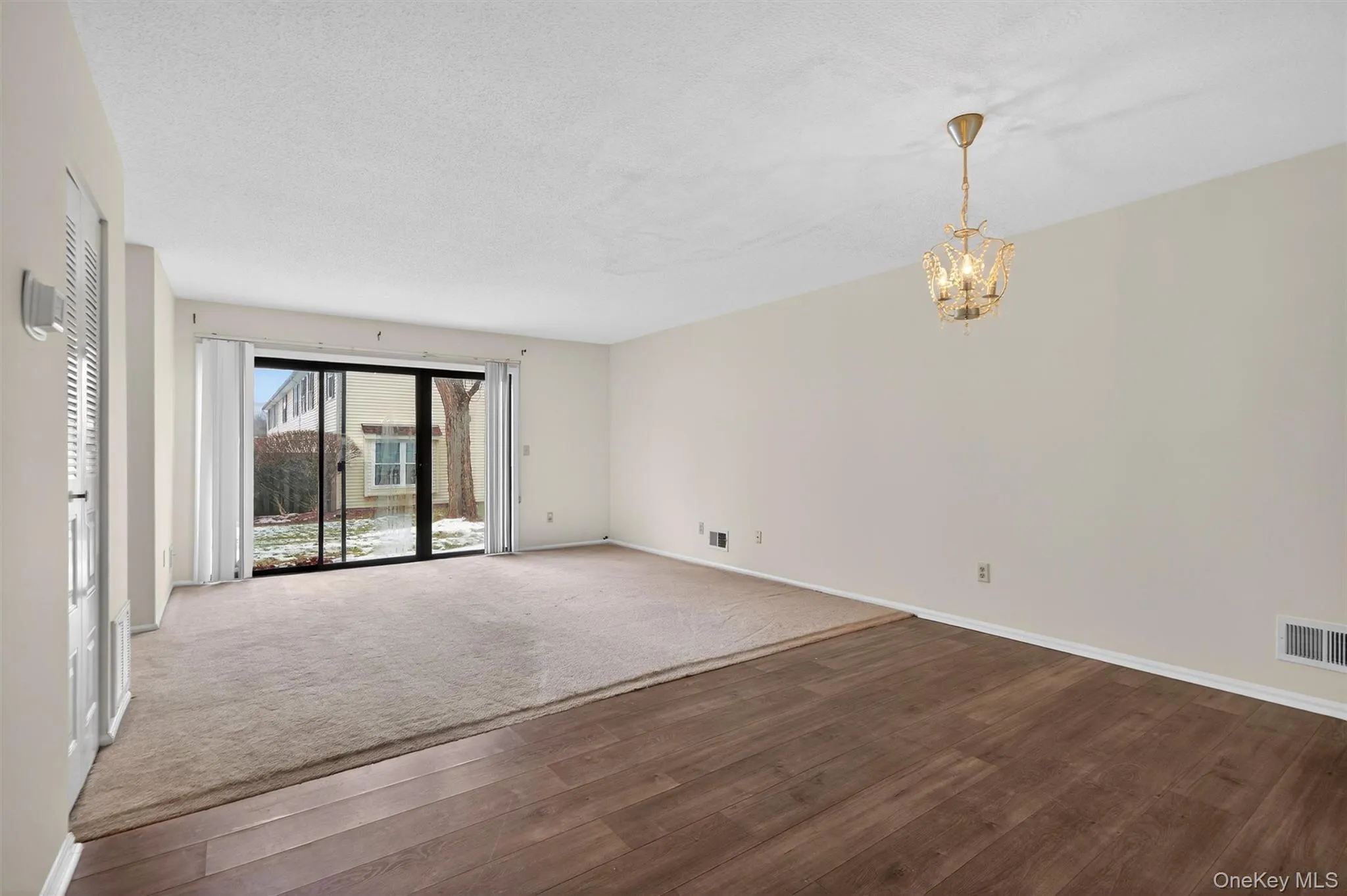 Empty room featuring dark wood-type flooring, a chandelier, and a textured ceiling Empty room featuring dark wood-type flooring, a chandelier, and a textured ceiling