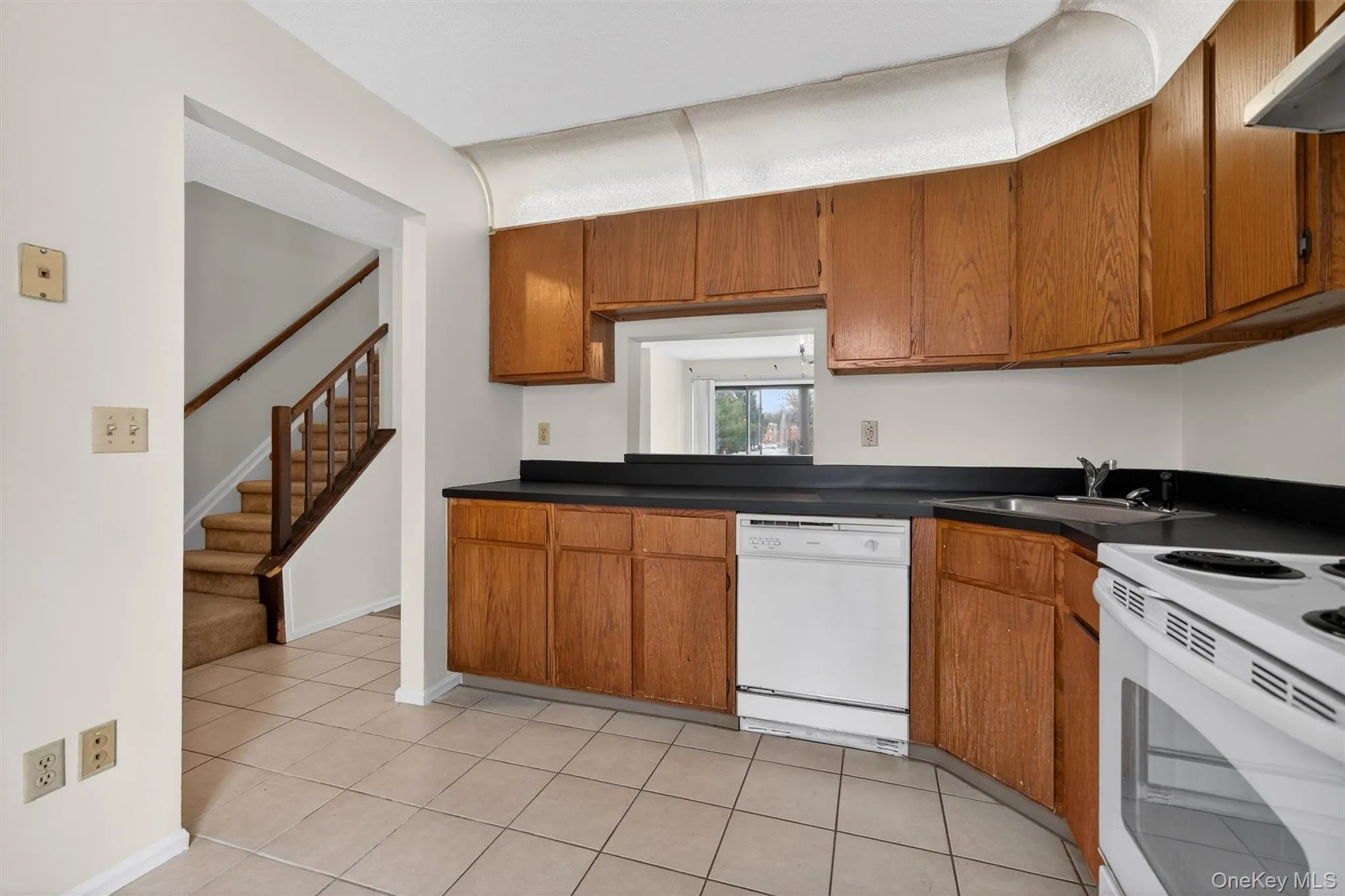 Kitchen with white appliances, brown cabinets, light tile patterned floors, and under cabinet range hood Kitchen with white appliances, brown cabinets, light tile patterned floors, and under cabinet range hood