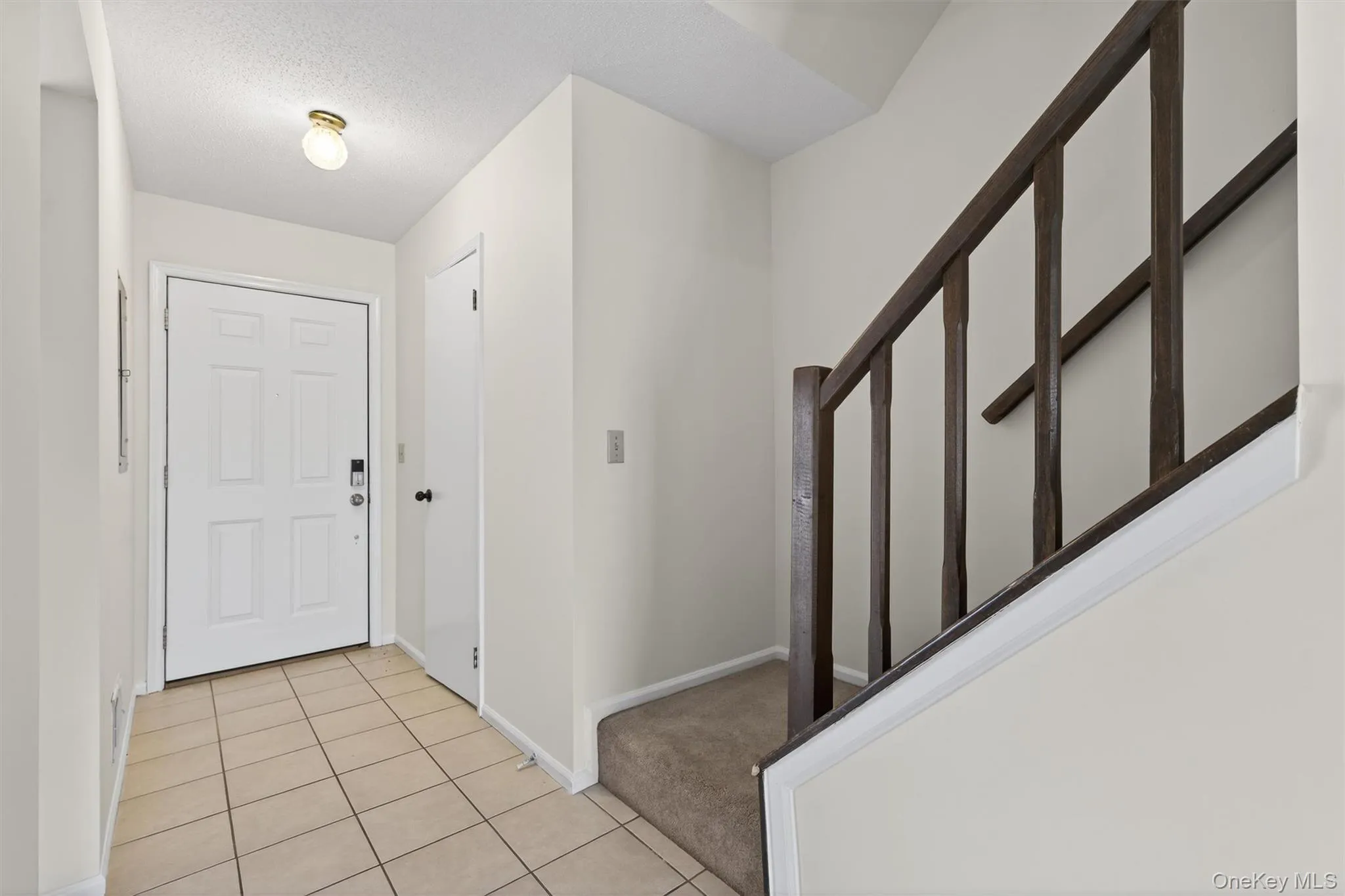 Entrance foyer with a textured ceiling, light tile patterned floors, stairs, and light carpet Entrance foyer with a textured ceiling, light tile patterned floors, stairs, and light carpet