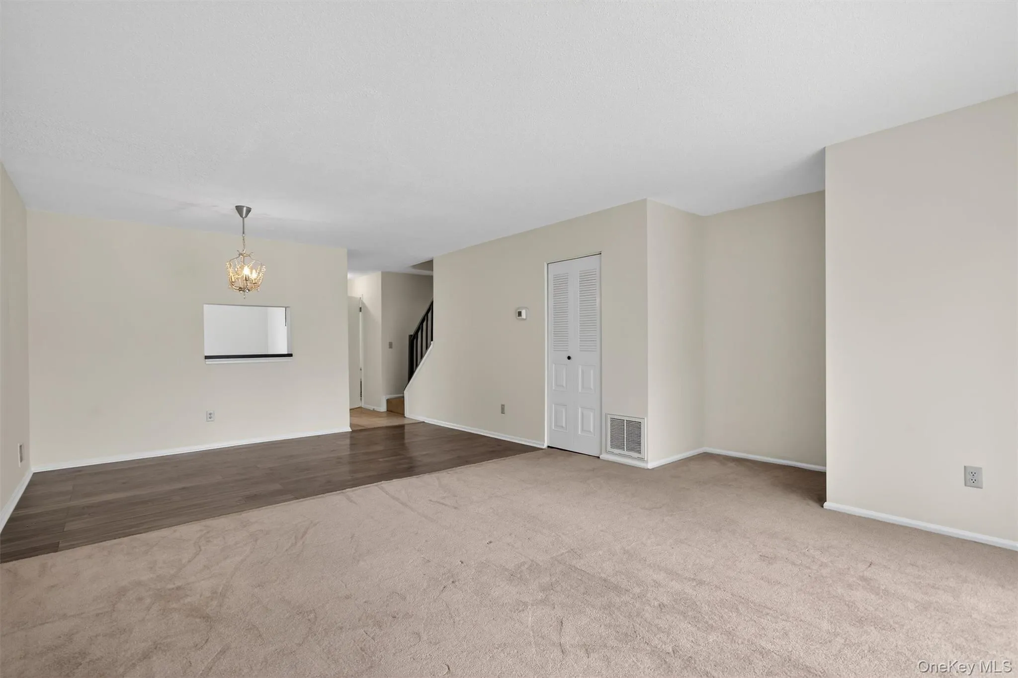 Unfurnished living room featuring carpet floors, a chandelier, and stairs Unfurnished living room featuring carpet floors, a chandelier, and stairs