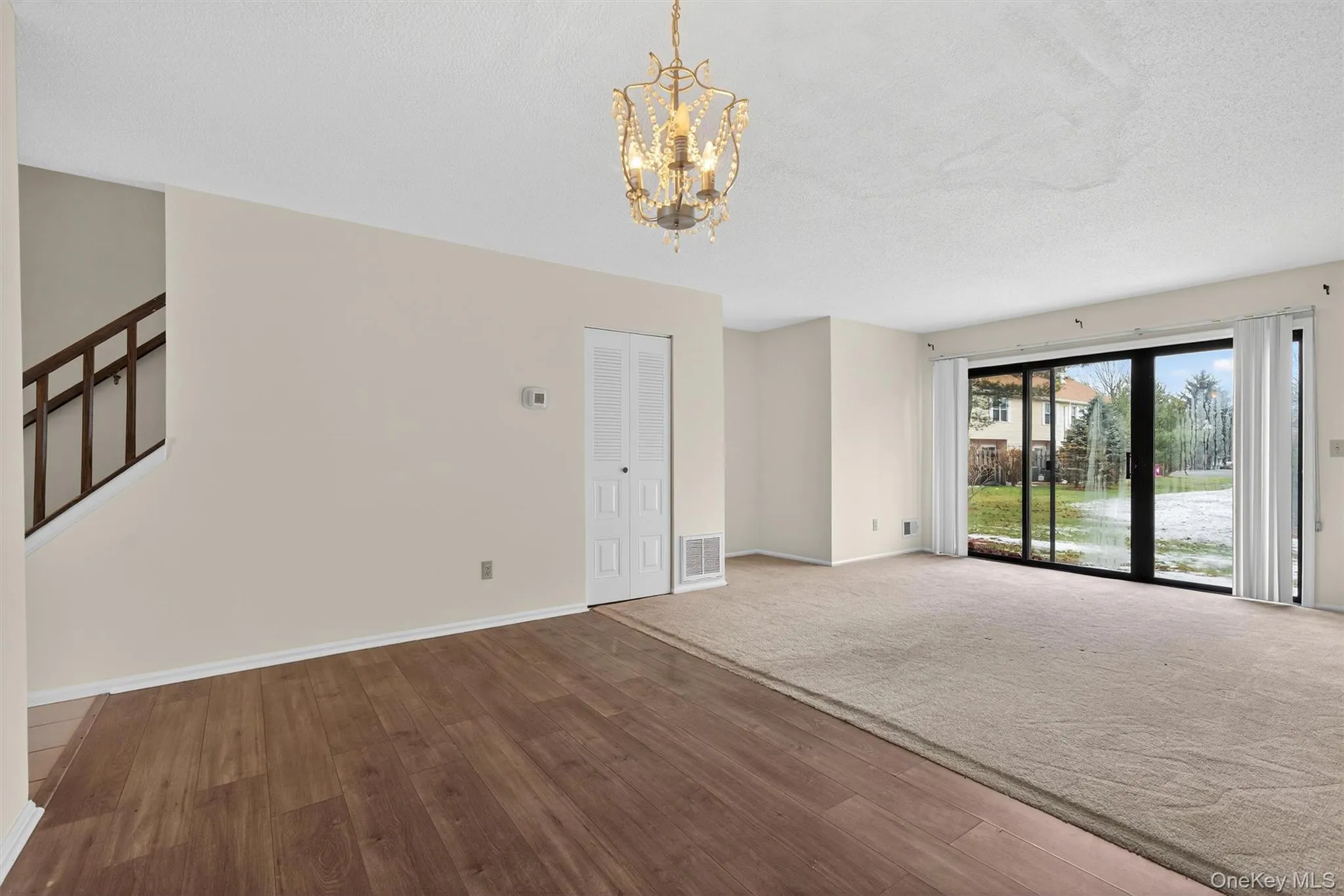 Empty room featuring wood finished floors, a chandelier, stairs, a textured ceiling, and carpet floors Empty room featuring wood finished floors, a chandelier, stairs, a textured ceiling, and carpet floors
