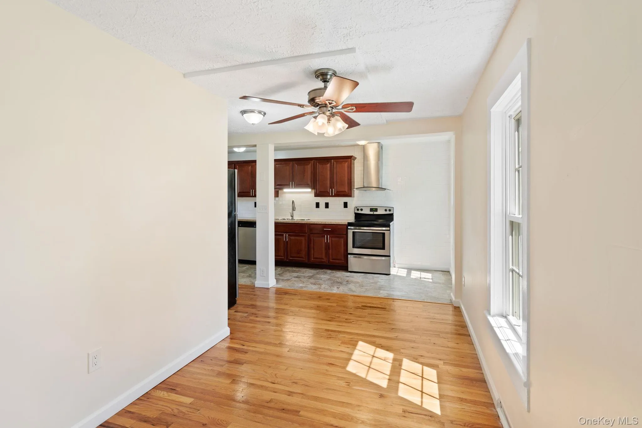 Kitchen featuring light countertops, appliances with stainless steel finishes, light wood-style floors, wall chimney range hood, and a textured ceiling Kitchen featuring light countertops, appliances with stainless steel finishes, light wood-style floors, wall chimney range hood, and a textured ceiling