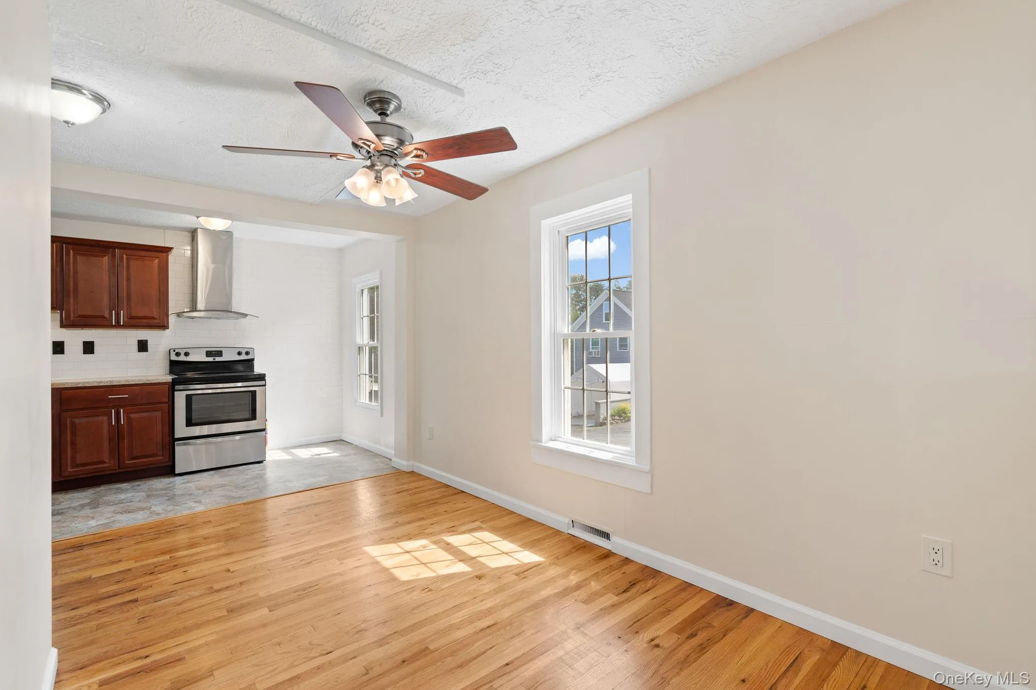 Kitchen with electric range, ceiling fan, wall chimney range hood, light countertops, and light wood finished floors Kitchen with electric range, ceiling fan, wall chimney range hood, light countertops, and light wood finished floors