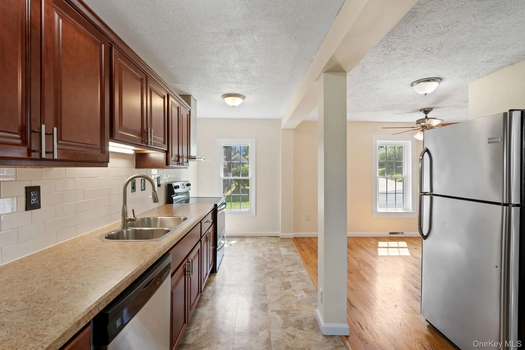 Kitchen with stainless steel appliances, a textured ceiling, backsplash, light wood-style flooring, and a ceiling fan Kitchen with stainless steel appliances, a textured ceiling, backsplash, light wood-style flooring, and a ceiling fan