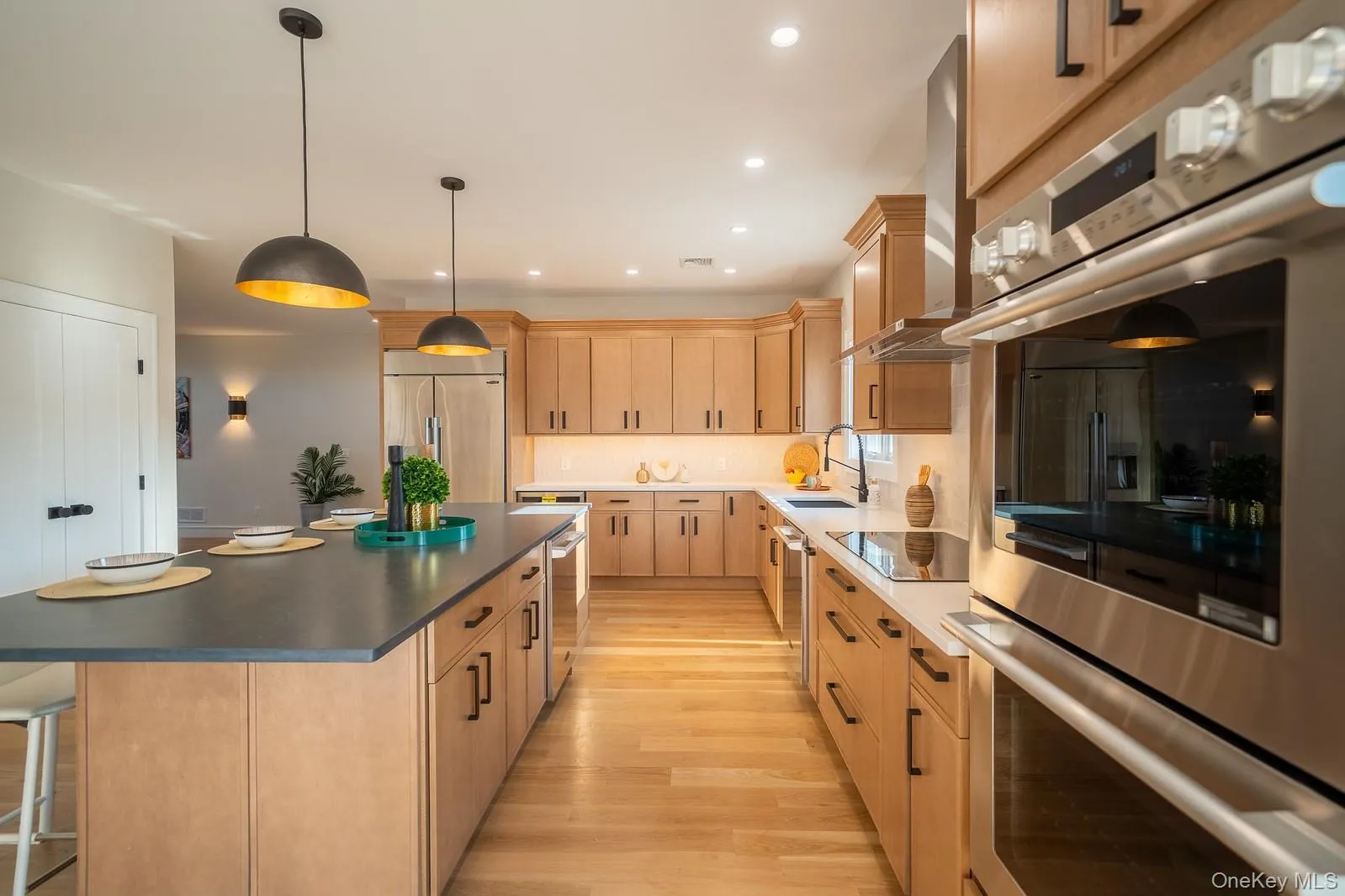 Kitchen featuring light brown cabinets, appliances with stainless steel finishes, a center island, light wood-type flooring, and wall chimney range hood Kitchen featuring light brown cabinets, appliances with stainless steel finishes, a center island, light wood-type flooring, and wall chimney range hood