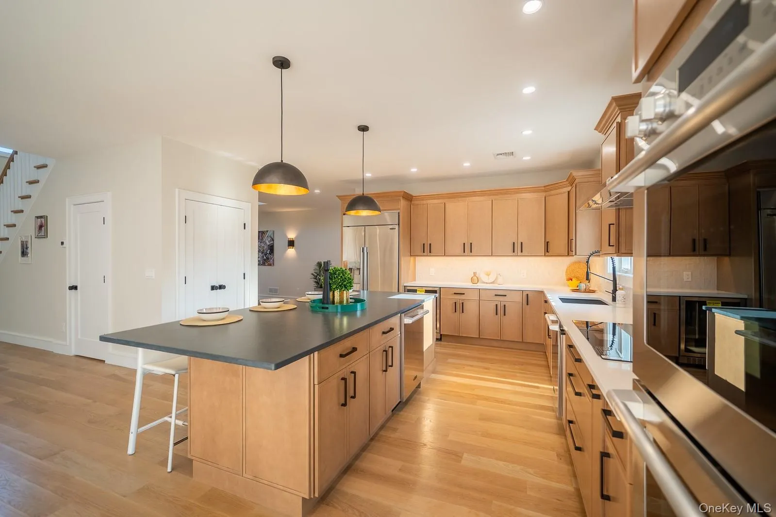 Kitchen with light wood-style floors, light brown cabinetry, a kitchen island, a breakfast bar, and appliances with stainless steel finishes Kitchen with light wood-style floors, light brown cabinetry, a kitchen island, a breakfast bar, and appliances with stainless steel finishes