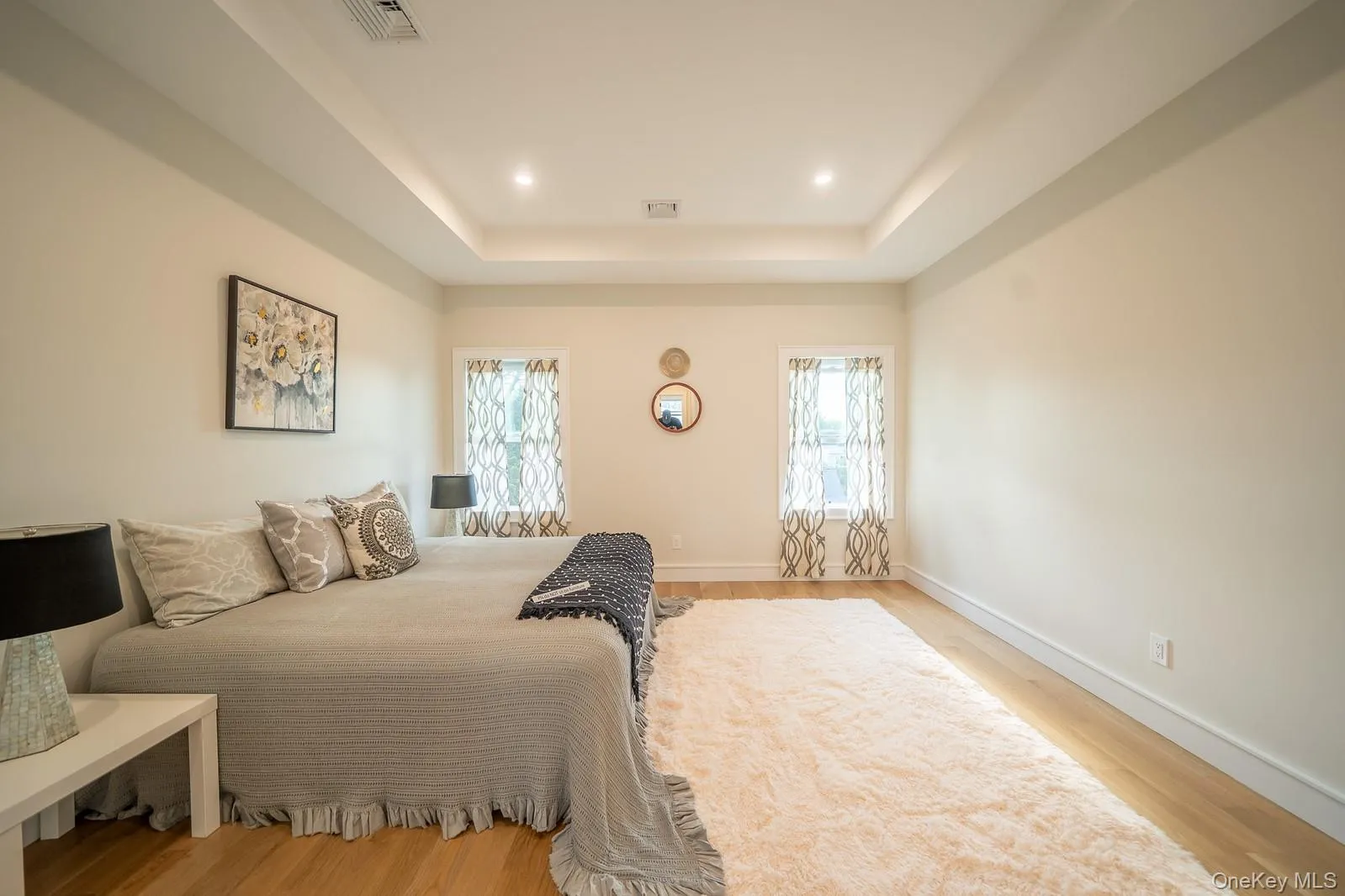Bedroom with multiple windows, a raised ceiling, light wood-style floors, and recessed lighting Bedroom with multiple windows, a raised ceiling, light wood-style floors, and recessed lighting