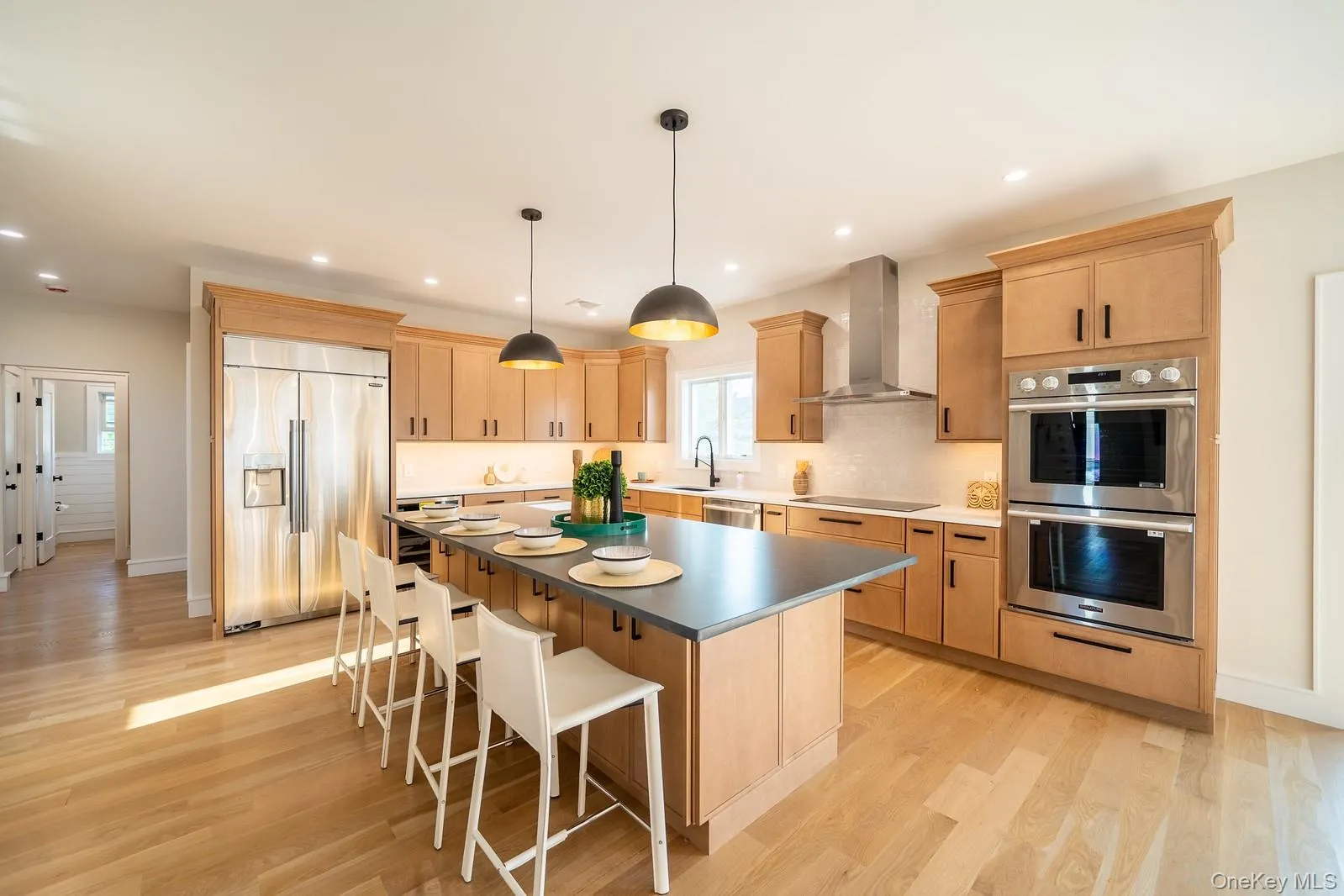 Kitchen with light brown cabinets, appliances with stainless steel finishes, a kitchen island, wall chimney exhaust hood, and recessed lighting Kitchen with light brown cabinets, appliances with stainless steel finishes, a kitchen island, wall chimney exhaust hood, and recessed lighting