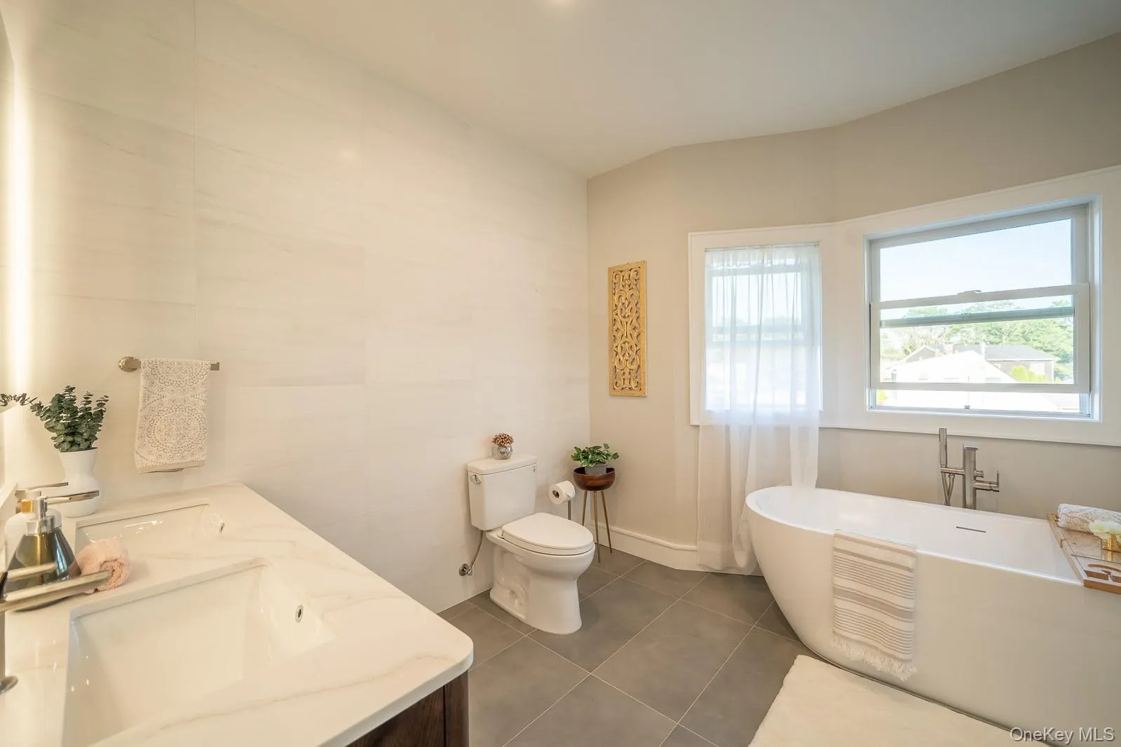 Full bathroom with tile patterned flooring, a freestanding tub, double vanity, and tile walls Full bathroom with tile patterned flooring, a freestanding tub, double vanity, and tile walls