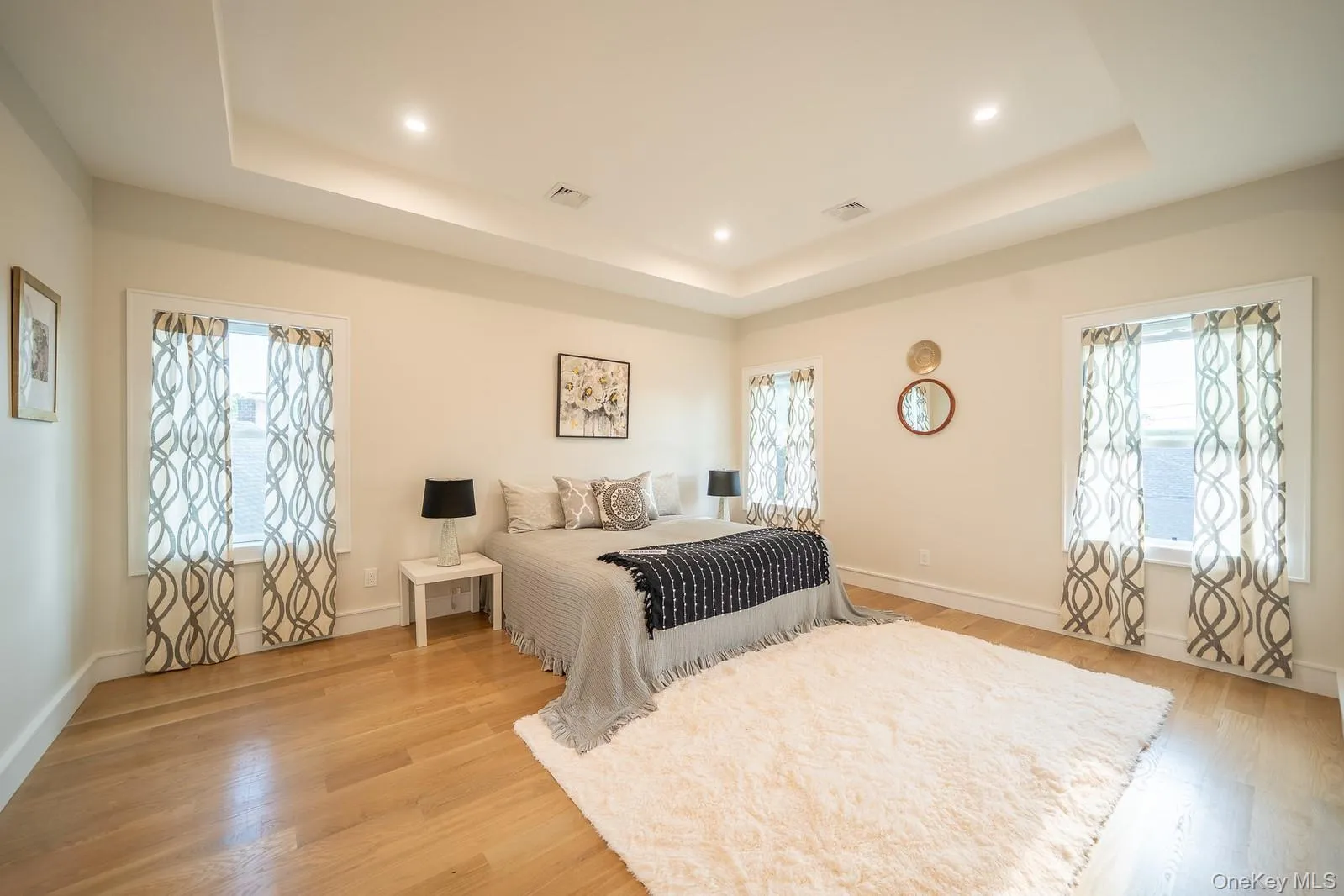 Bedroom with a tray ceiling, light wood-type flooring, and recessed lighting Bedroom with a tray ceiling, light wood-type flooring, and recessed lighting