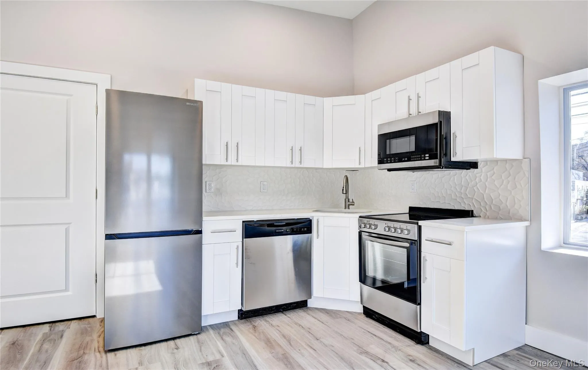 Kitchen with stainless steel appliances, white cabinets, backsplash, and light wood finished floors Kitchen with stainless steel appliances, white cabinets, backsplash, and light wood finished floors