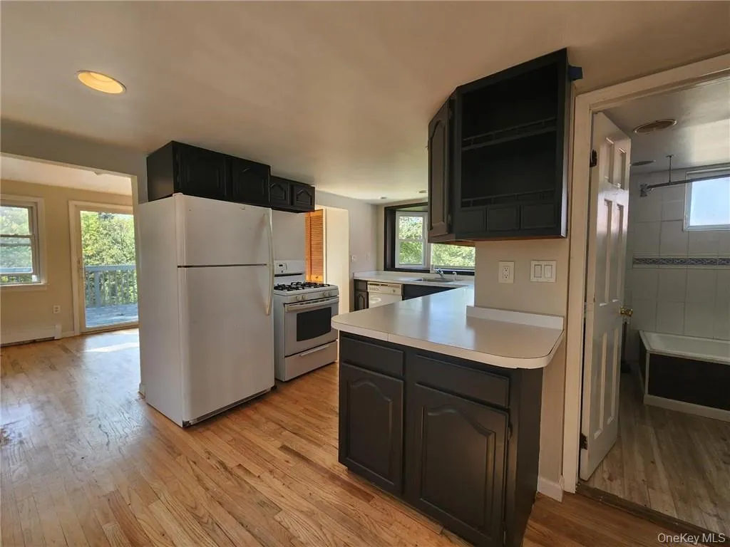 Kitchen with white appliances, dark cabinetry, light countertops, light wood-type flooring, and a baseboard radiator Kitchen with white appliances, dark cabinetry, light countertops, light wood-type flooring, and a baseboard radiator