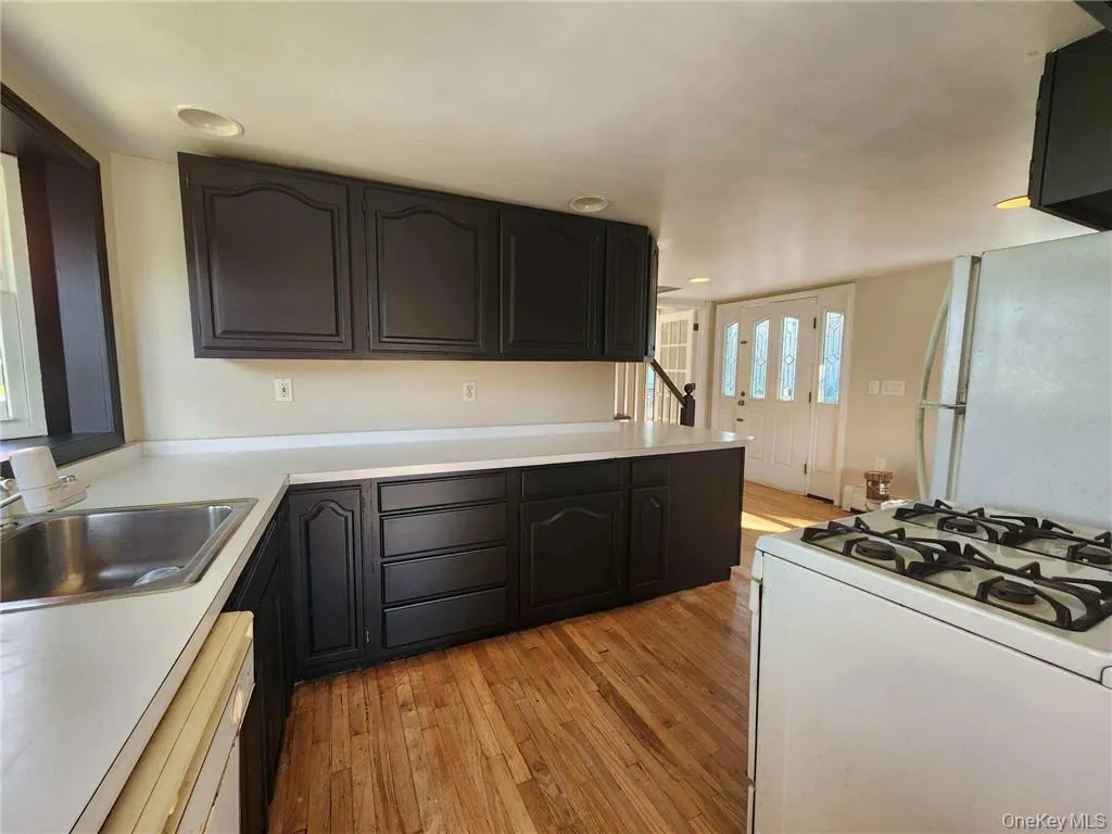 Kitchen with white appliances, light wood-type flooring, light countertops, dark cabinets, and recessed lighting Kitchen with white appliances, light wood-type flooring, light countertops, dark cabinets, and recessed lighting