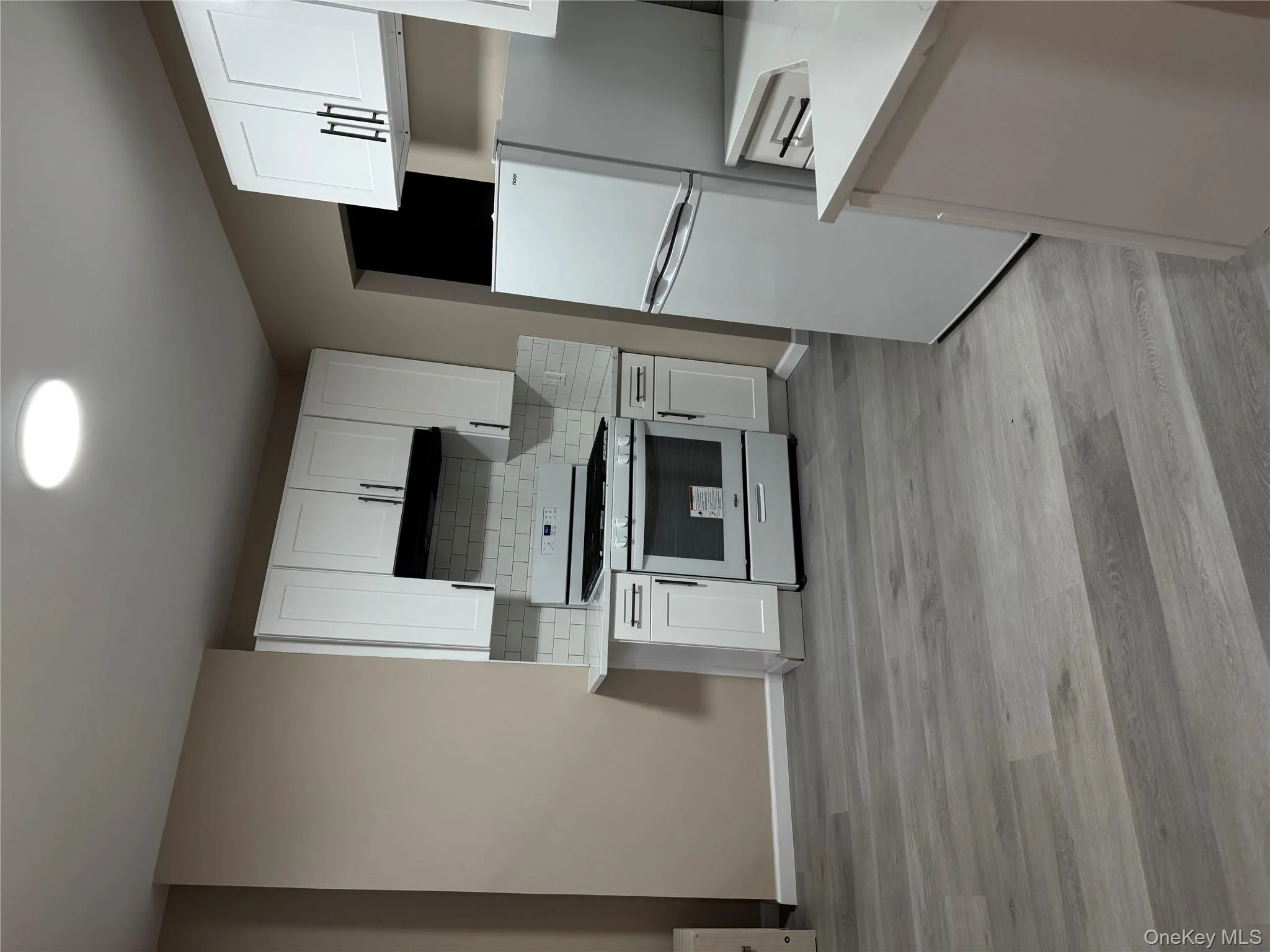 Kitchen featuring white gas stove, stainless steel refrigerator, backsplash, white cabinetry, and light wood-style floors Kitchen featuring white gas stove, stainless steel refrigerator, backsplash, white cabinetry, and light wood-style floors