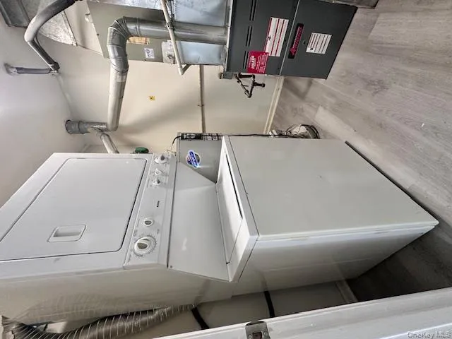 Laundry area with heating unit, light wood-style flooring, and stacked washer / drying machine Laundry area with heating unit, light wood-style flooring, and stacked washer / drying machine