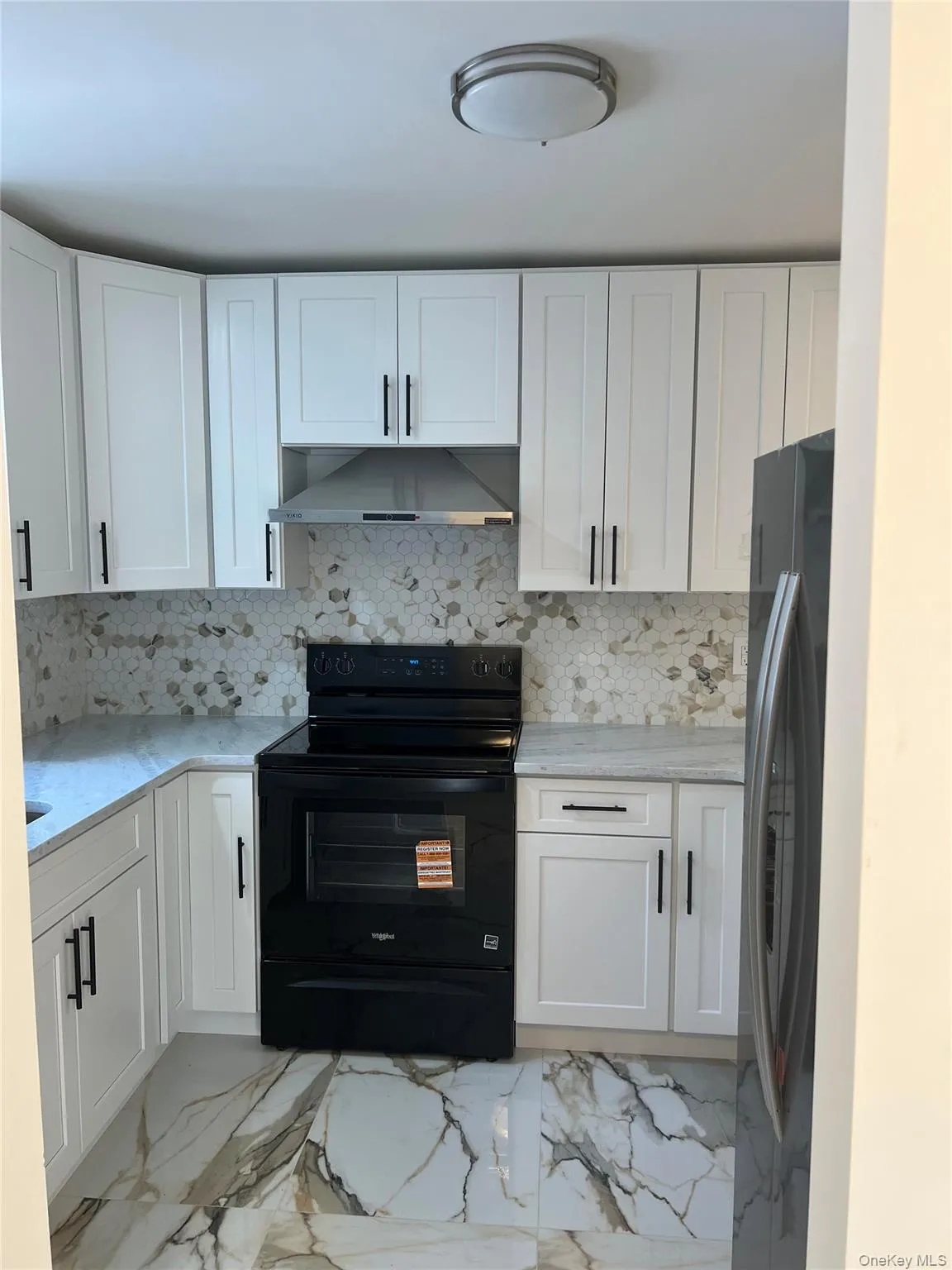 Kitchen with black / electric stove, white cabinets, light marble finish floors, light stone countertops, and decorative backsplash Kitchen with black / electric stove, white cabinets, light marble finish floors, light stone countertops, and decorative backsplash