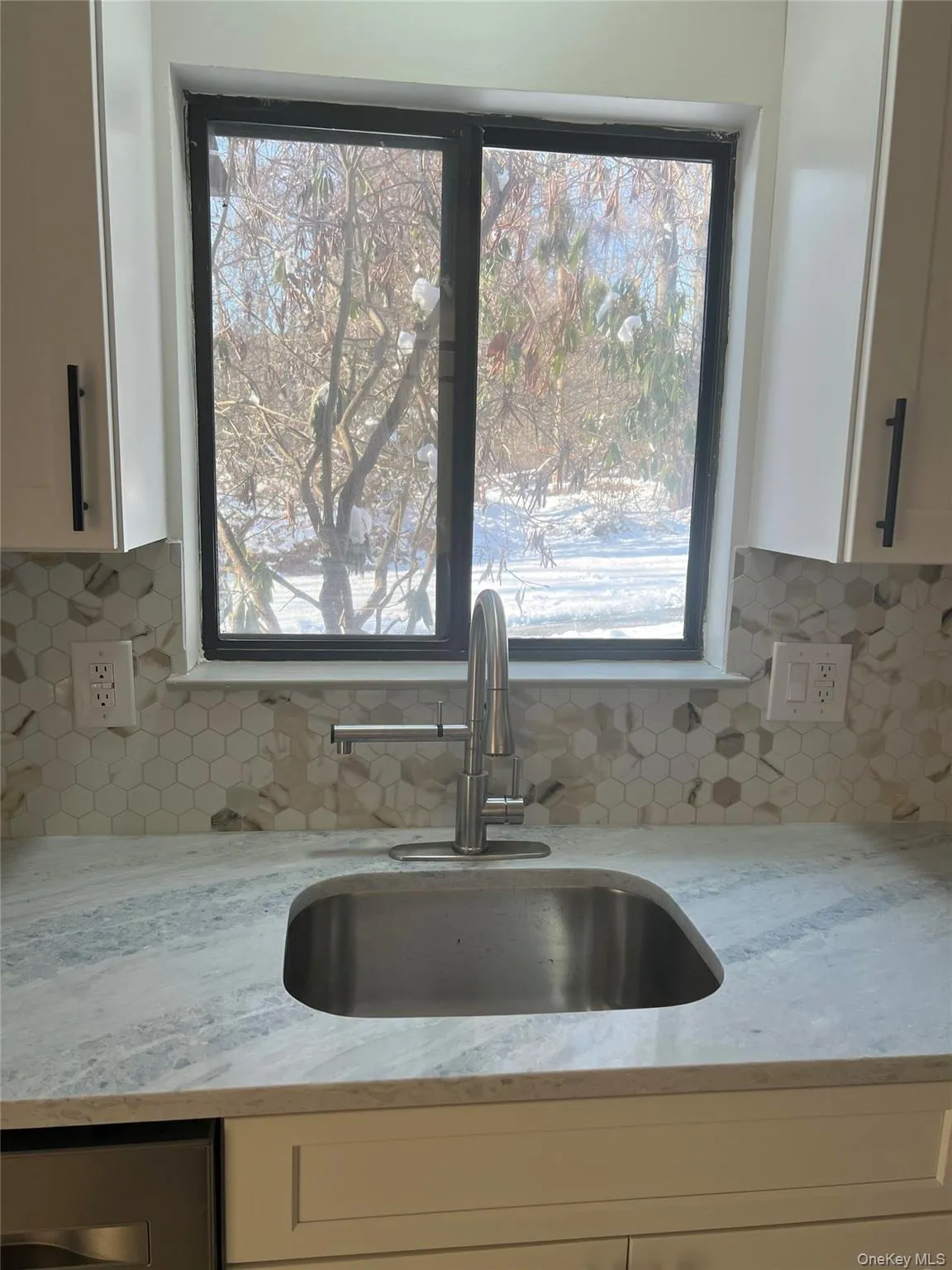 Kitchen view of light stone countertops, decorative backsplash, and white cabinetry Kitchen view of light stone countertops, decorative backsplash, and white cabinetry