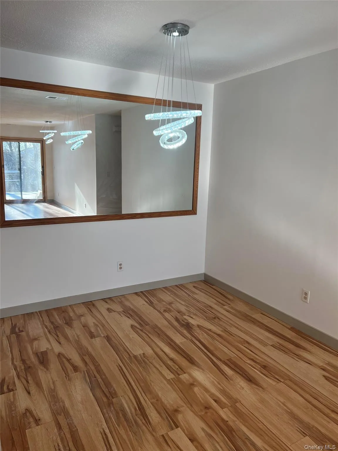 Empty room featuring wood finished floors, a chandelier, and a textured ceiling Empty room featuring wood finished floors, a chandelier, and a textured ceiling