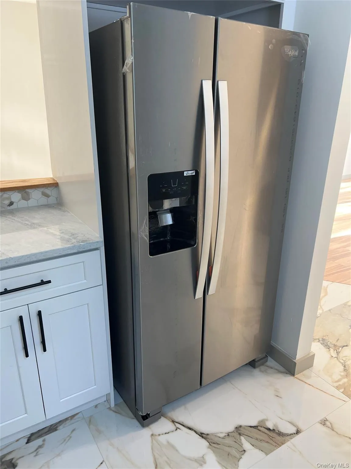 Kitchen view of stainless steel fridge, light stone counters, and white cabinetry Kitchen view of stainless steel fridge, light stone counters, and white cabinetry