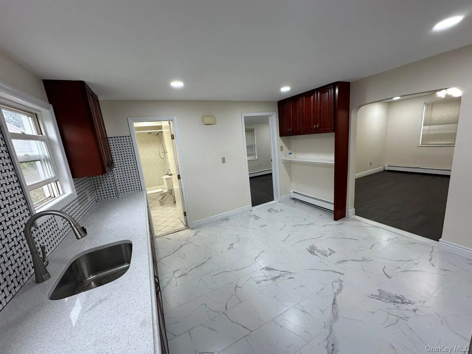 Kitchen featuring light marble finish floors, light stone counters, dark brown cabinets, baseboard heating, and arched walkways Kitchen featuring light marble finish floors, light stone counters, dark brown cabinets, baseboard heating, and arched walkways