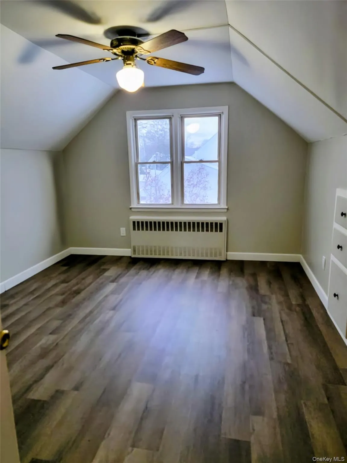 Additional living space featuring lofted ceiling, radiator heating unit, dark wood finished floors, and a ceiling fan Additional living space featuring lofted ceiling, radiator heating unit, dark wood finished floors, and a ceiling fan