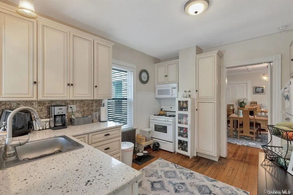 Kitchen with cream cabinetry, white appliances, light wood-type flooring, and light stone counters Kitchen with cream cabinetry, white appliances, light wood-type flooring, and light stone counters