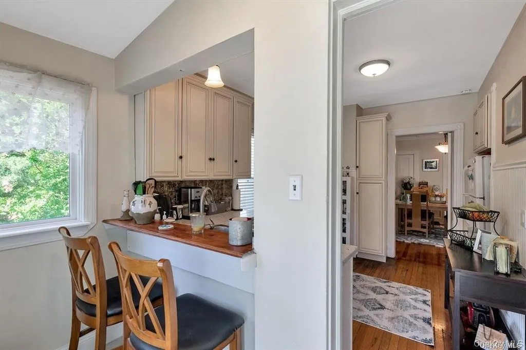 Kitchen featuring cream cabinetry, dark wood-style floors, butcher block countertops, a kitchen bar, and a desk Kitchen featuring cream cabinetry, dark wood-style floors, butcher block countertops, a kitchen bar, and a desk
