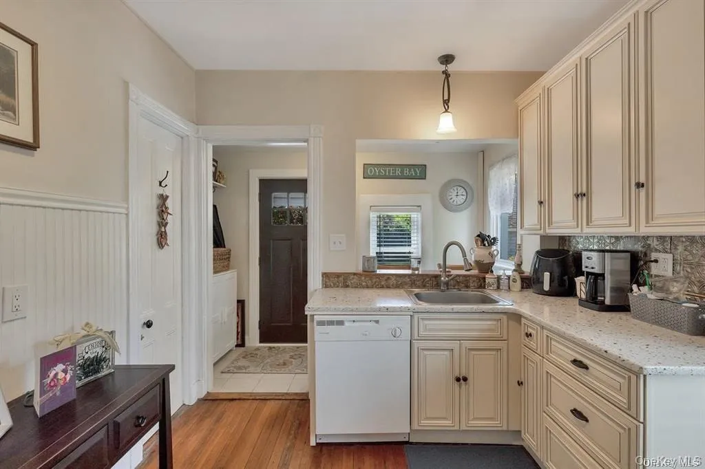 Kitchen featuring cream cabinets, white dishwasher, hanging light fixtures, light wood-type flooring, and light stone counters Kitchen featuring cream cabinets, white dishwasher, hanging light fixtures, light wood-type flooring, and light stone counters