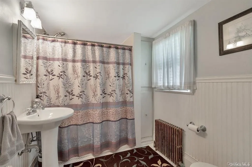 Bathroom featuring wainscoting, radiator heating unit, wood walls, curtained shower, and a decorative wall Bathroom featuring wainscoting, radiator heating unit, wood walls, curtained shower, and a decorative wall