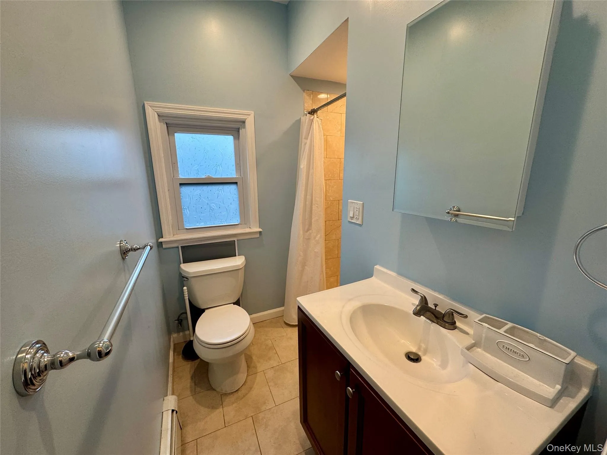 Full bath with vanity, a shower with shower curtain, light tile patterned floors, and a baseboard radiator Full bath with vanity, a shower with shower curtain, light tile patterned floors, and a baseboard radiator