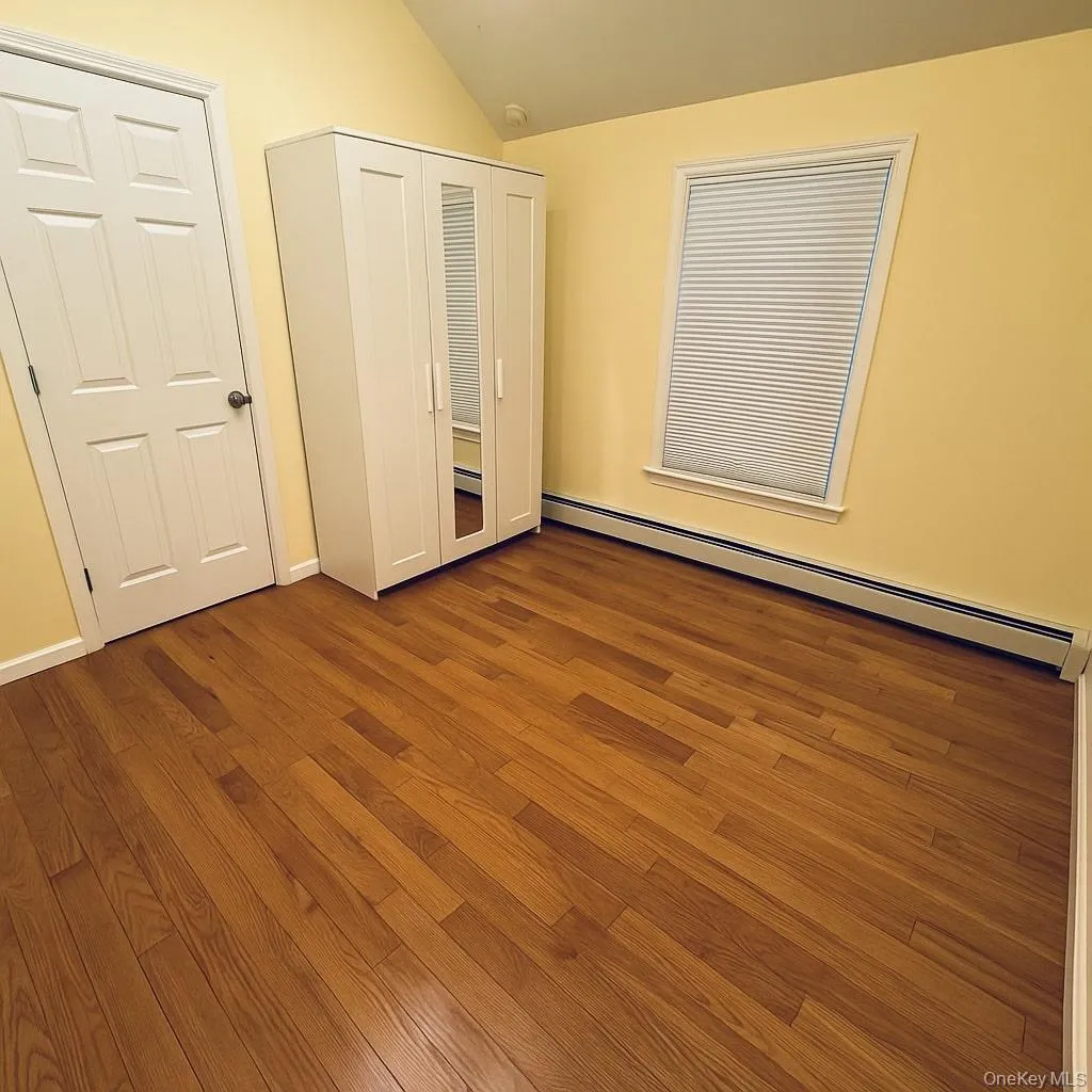 Unfurnished bedroom featuring baseboard heating, wood finished floors, vaulted ceiling, and a closet Unfurnished bedroom featuring baseboard heating, wood finished floors, vaulted ceiling, and a closet