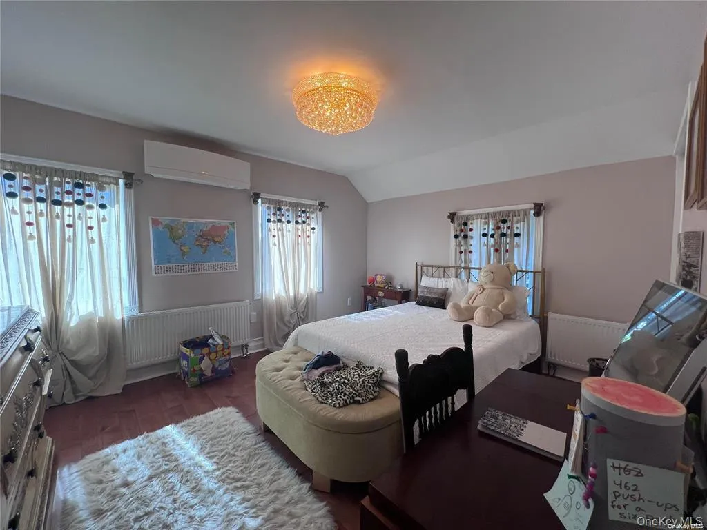 Bedroom featuring radiator, vaulted ceiling, dark wood finished floors, and a wall mounted air conditioner Bedroom featuring radiator, vaulted ceiling, dark wood finished floors, and a wall mounted air conditioner