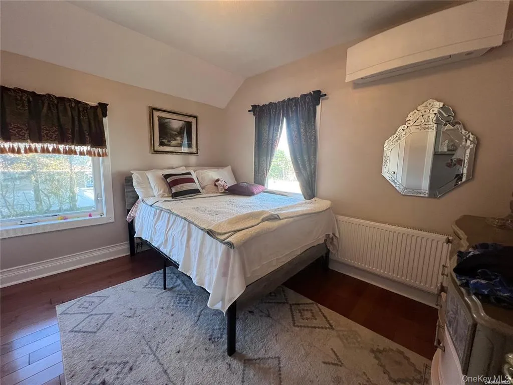 Bedroom with radiator heating unit, a wall mounted AC, vaulted ceiling, and dark wood-style flooring Bedroom with radiator heating unit, a wall mounted AC, vaulted ceiling, and dark wood-style flooring