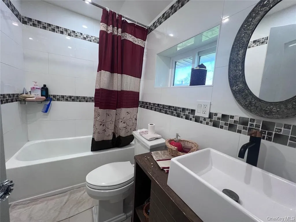 Bathroom featuring vanity, shower / tub combo, and tile walls Bathroom featuring vanity, shower / tub combo, and tile walls