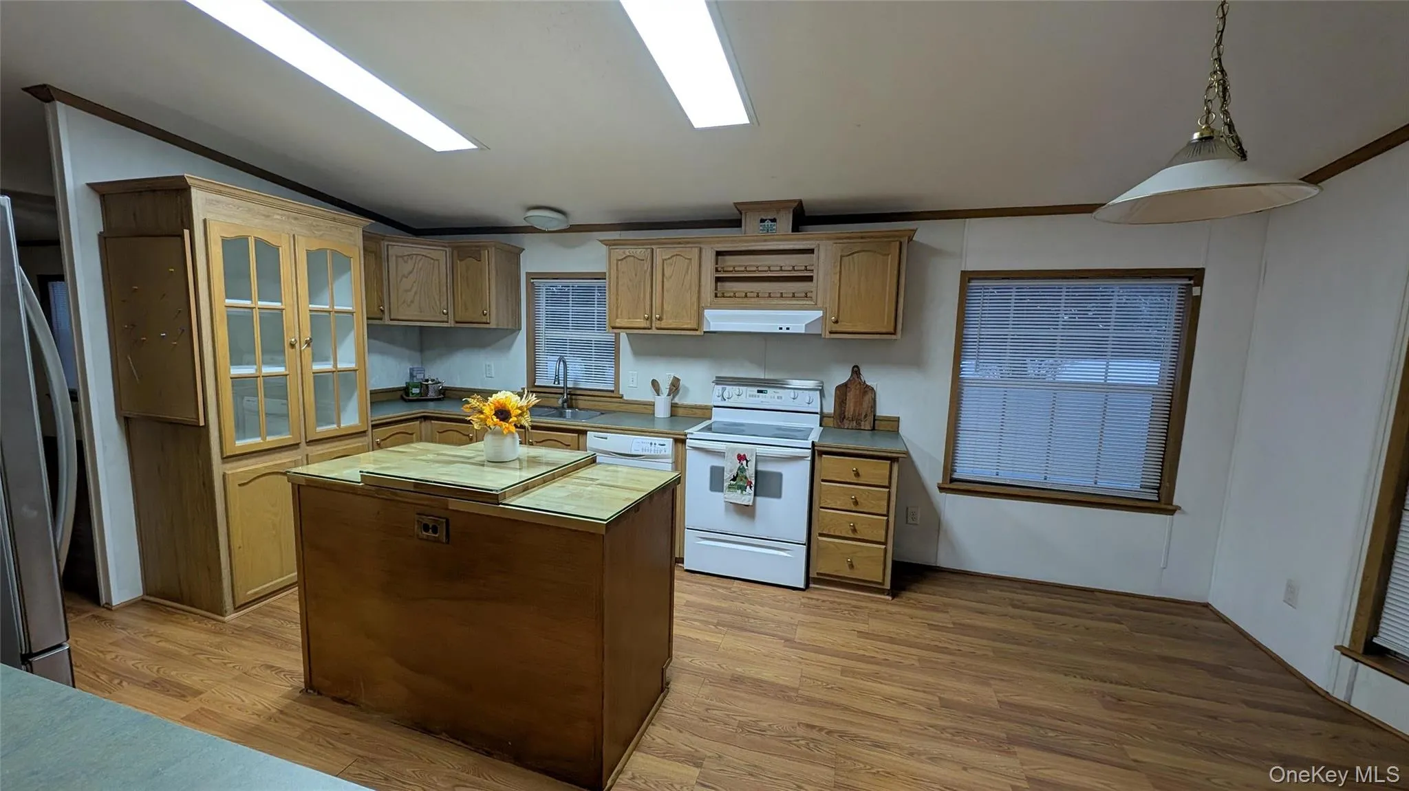 Kitchen with a center island, glass insert cabinets, white appliances, light wood-style flooring, and crown molding Kitchen with a center island, glass insert cabinets, white appliances, light wood-style flooring, and crown molding