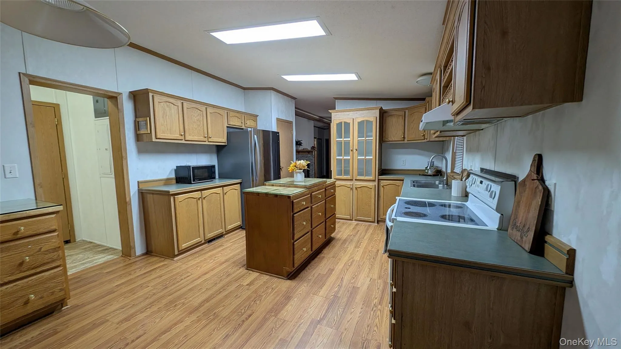 Kitchen with a kitchen island, light wood-type flooring, white electric stove, ornamental molding, and black microwave Kitchen with a kitchen island, light wood-type flooring, white electric stove, ornamental molding, and black microwave