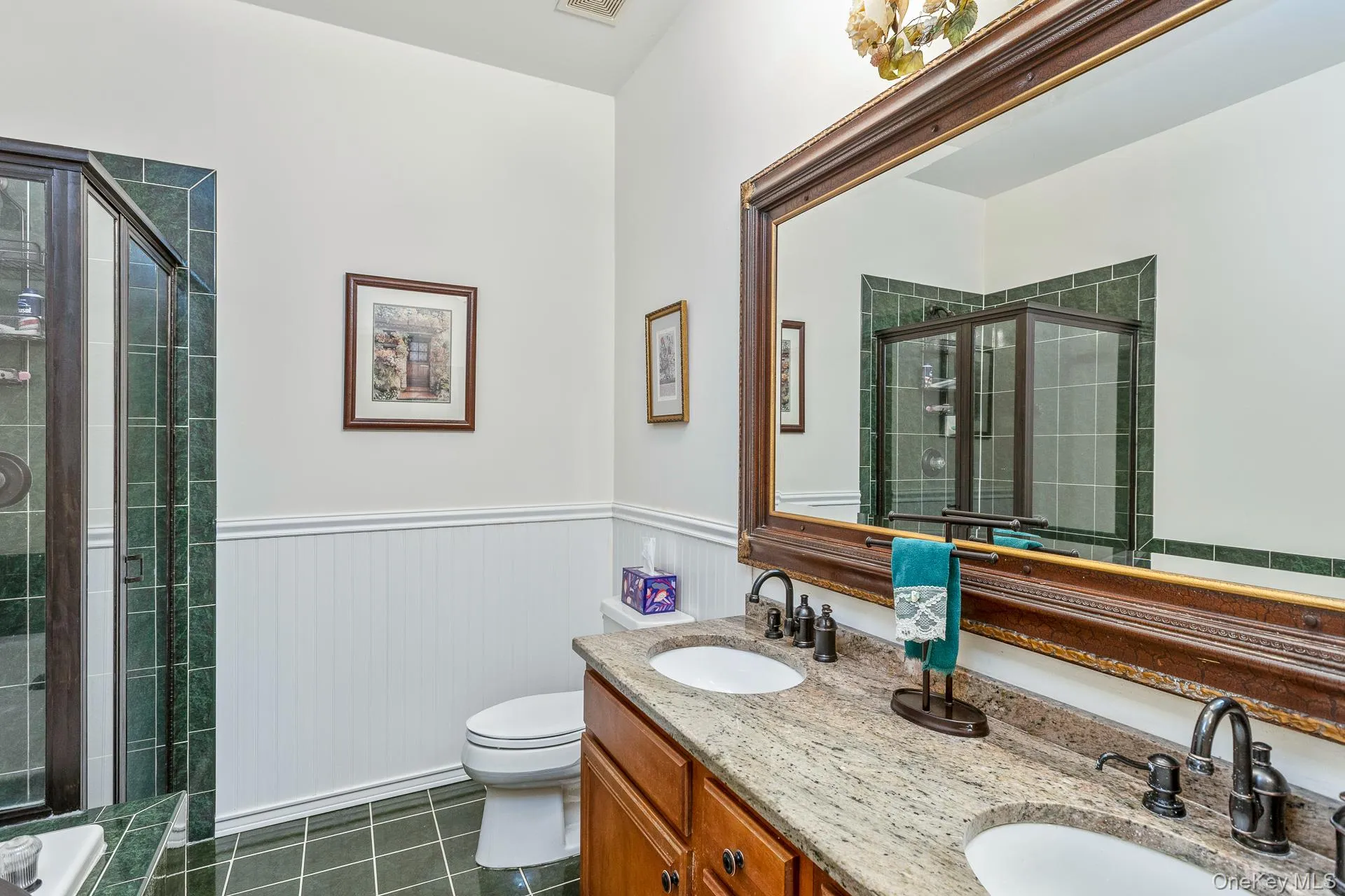 Full bathroom featuring a stall shower, double vanity, a wainscoted wall, and dark tile patterned floors Full bathroom featuring a stall shower, double vanity, a wainscoted wall, and dark tile patterned floors