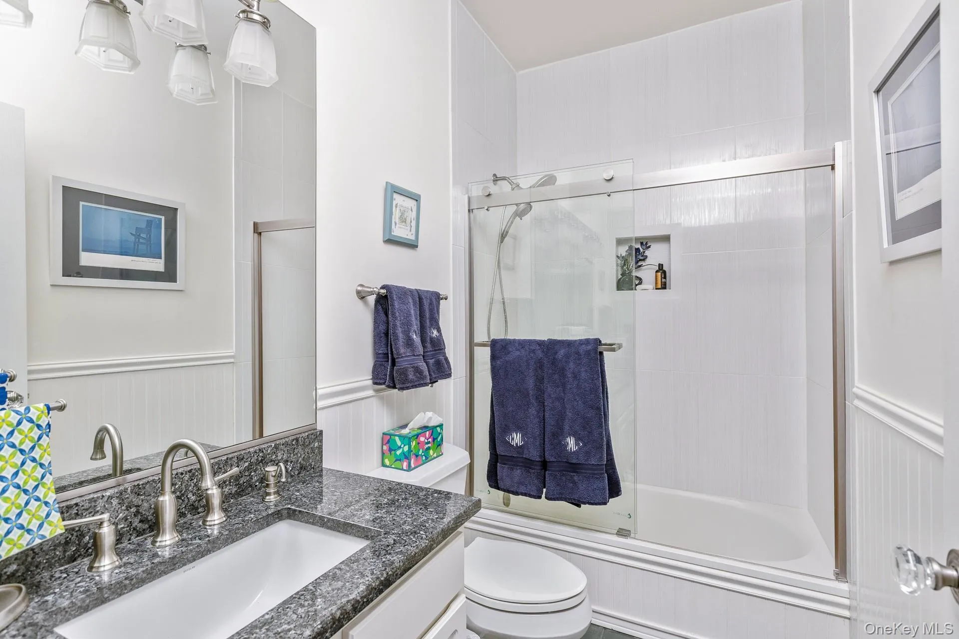 Bathroom featuring vanity, wainscoting, bath / shower combo with glass door, and a decorative wall Bathroom featuring vanity, wainscoting, bath / shower combo with glass door, and a decorative wall