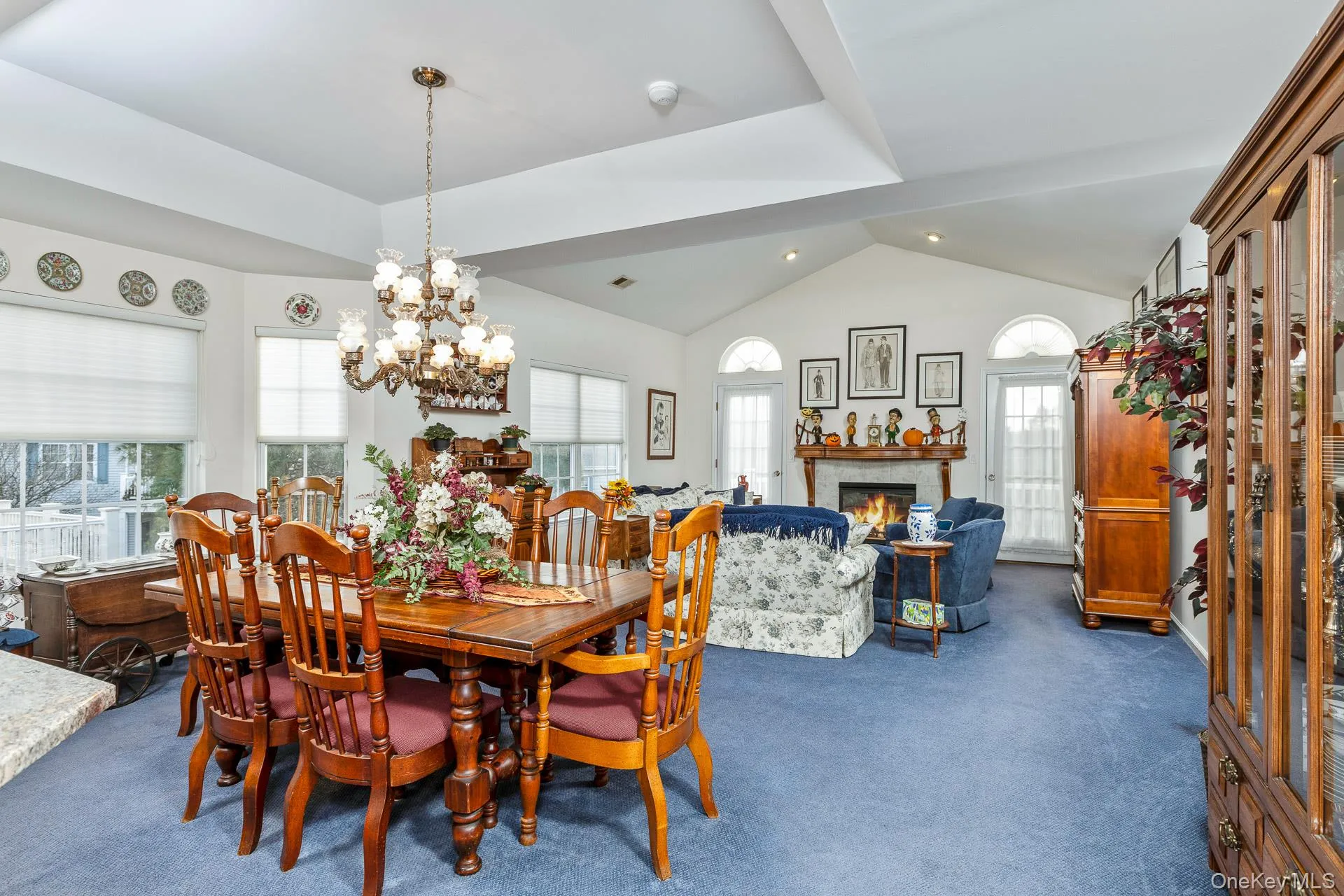 Dining room with a lit fireplace, dark carpet, vaulted ceiling, and a chandelier Dining room with a lit fireplace, dark carpet, vaulted ceiling, and a chandelier