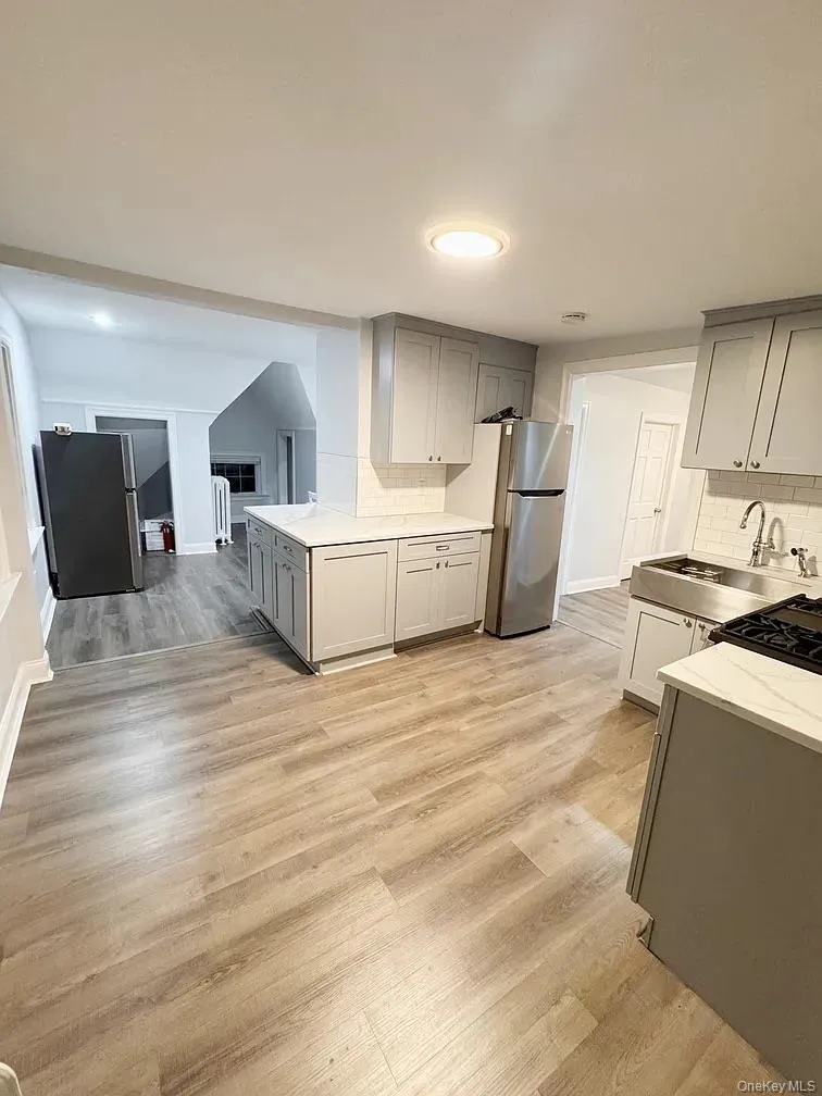 Kitchen with gray cabinetry, light wood-type flooring, and decorative backsplash Kitchen with gray cabinetry, light wood-type flooring, and decorative backsplash