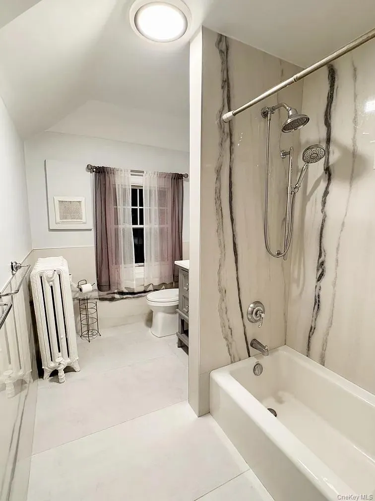 Bathroom with shower / bath combination with curtain, radiator heating unit, and lofted ceiling Bathroom with shower / bath combination with curtain, radiator heating unit, and lofted ceiling